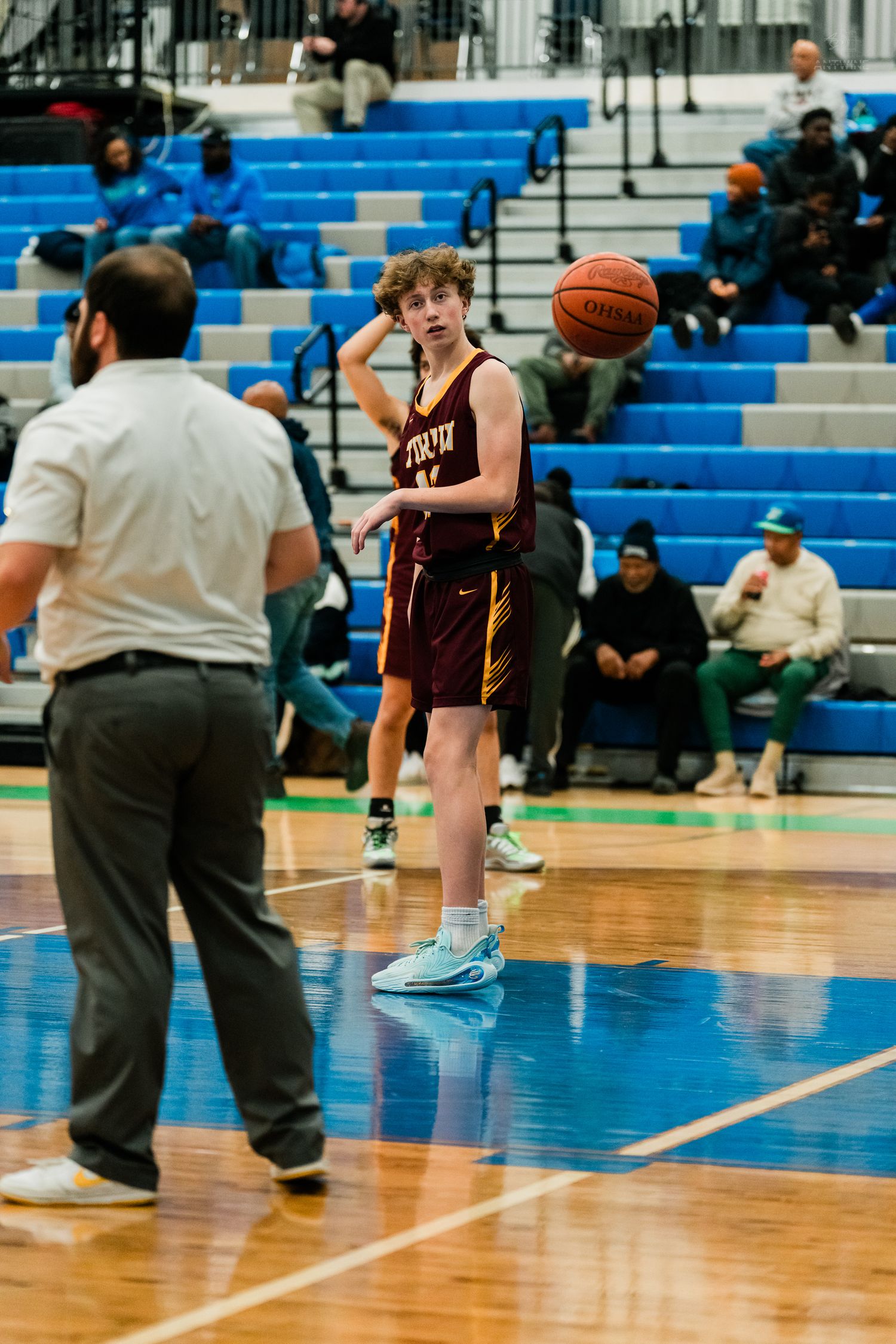 A high school basketball player in a maroon jersey passes the ball to a referee on the court.