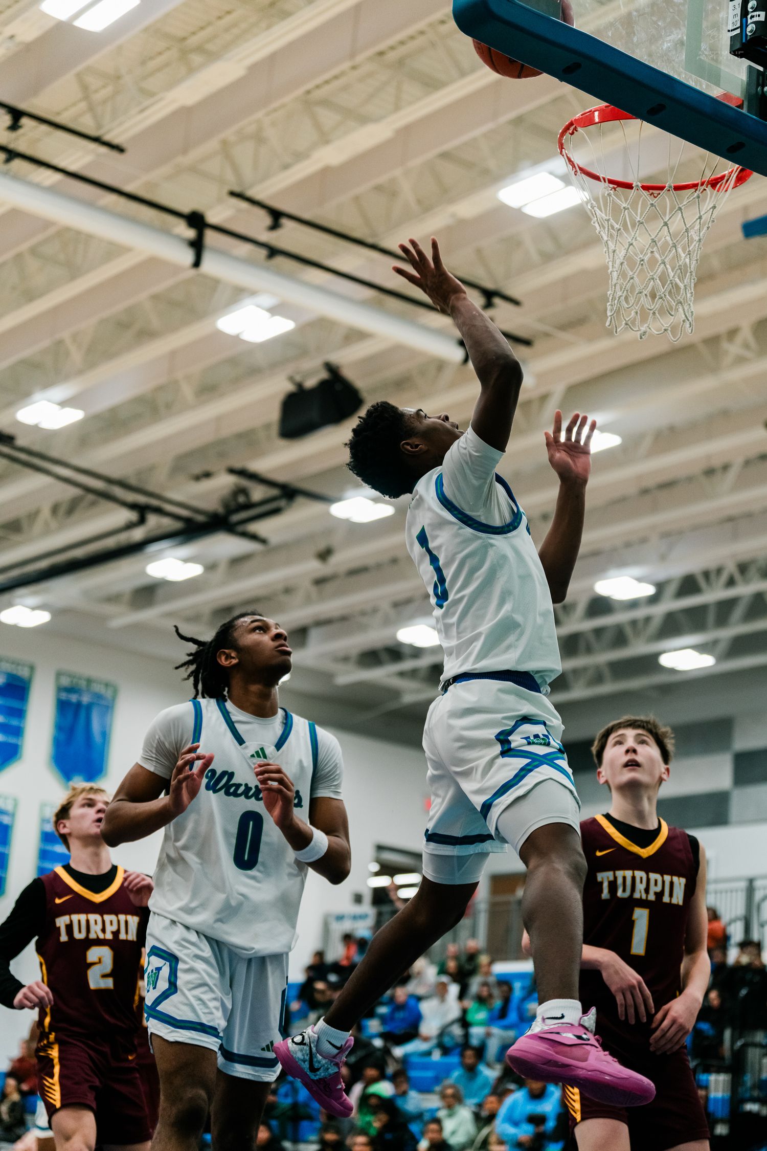 Warriors basketball player leaps for a layup over Turpin defenders during an intense high school game.