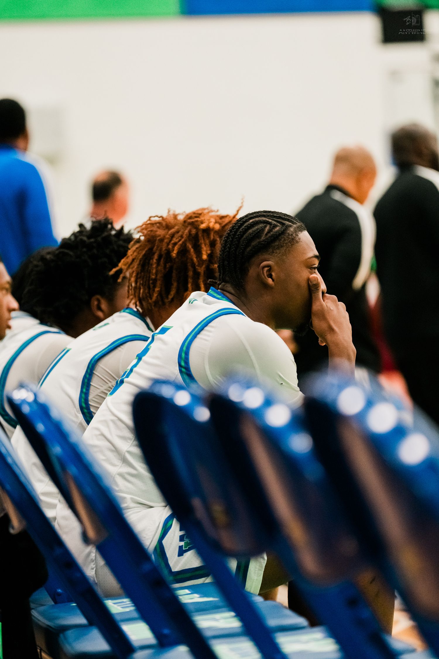 High school basketball player with braids sitting on bench during indoor game.