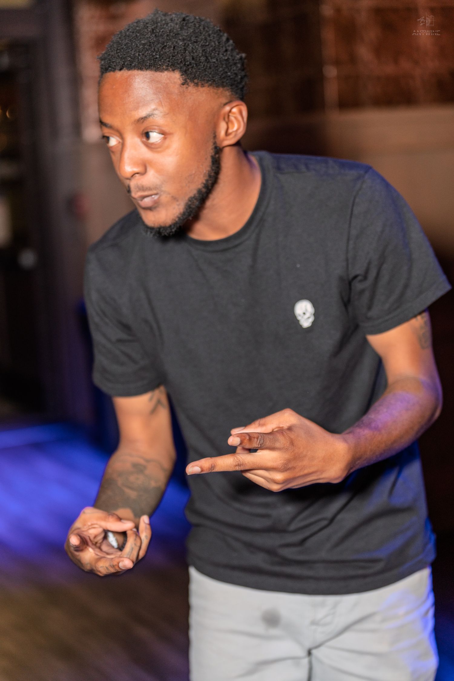 Tattooed man in a black skull t-shirt pointing fingers while performing at a bar event.