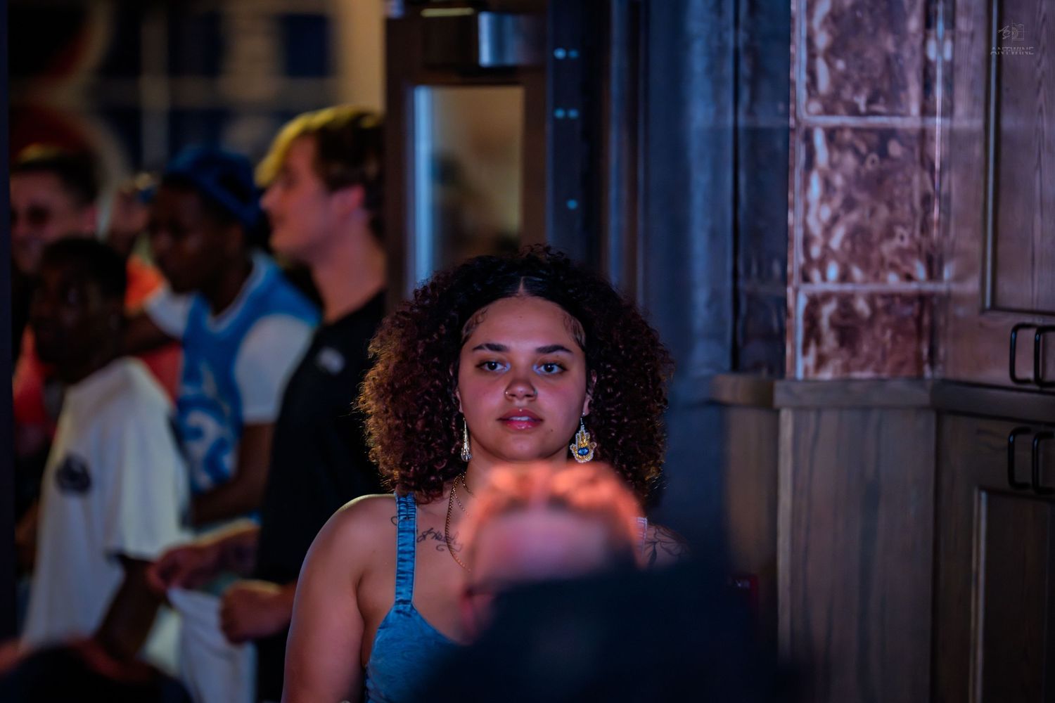 Young woman with curly hair and hoop earrings looking up at a lively nightclub event.