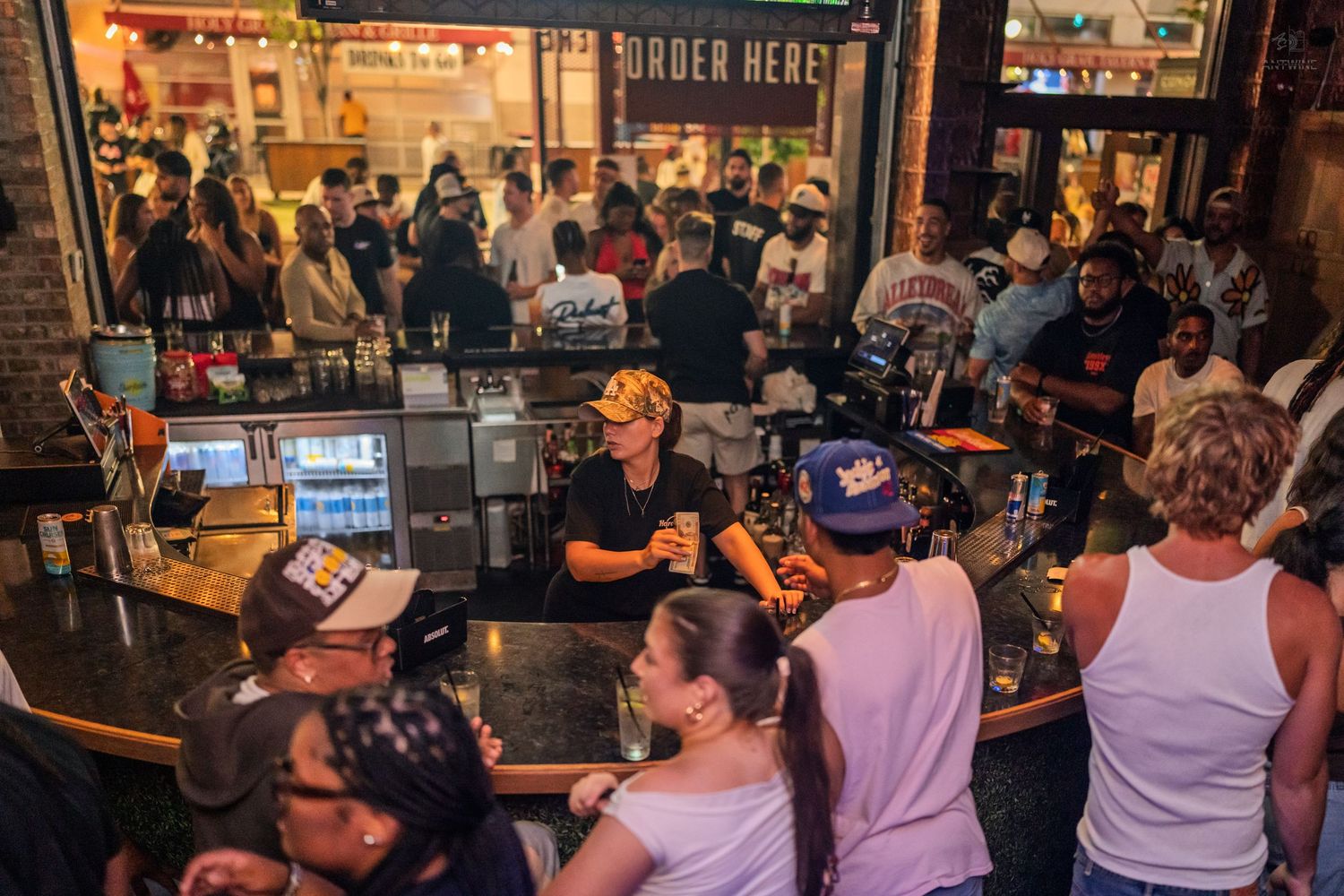 Busy bar with bartenders serving drinks to a large diverse crowd at a popular nightclub venue.
