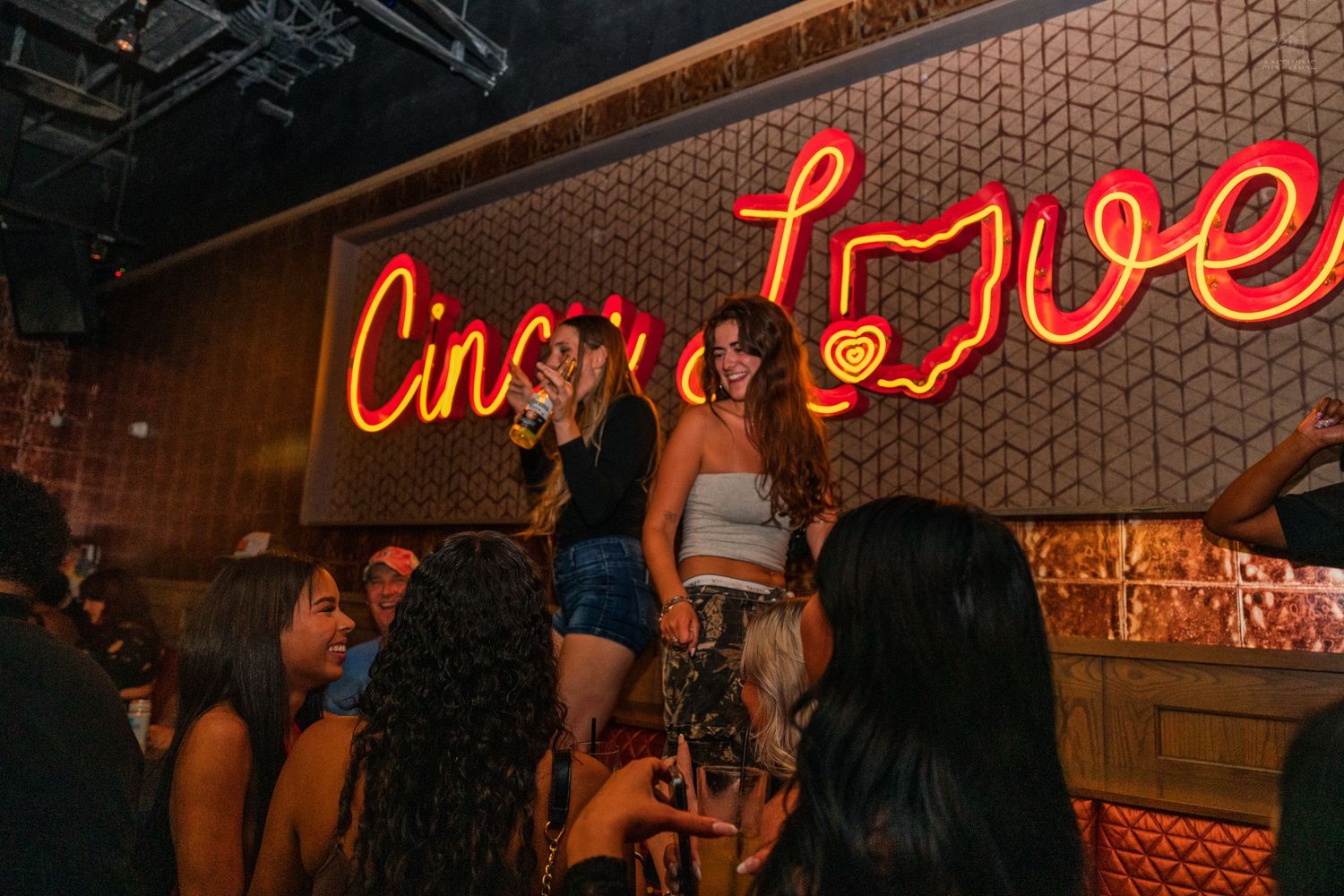 Group of women standing under the Cincinnati Love neon sign at a nightclub.
