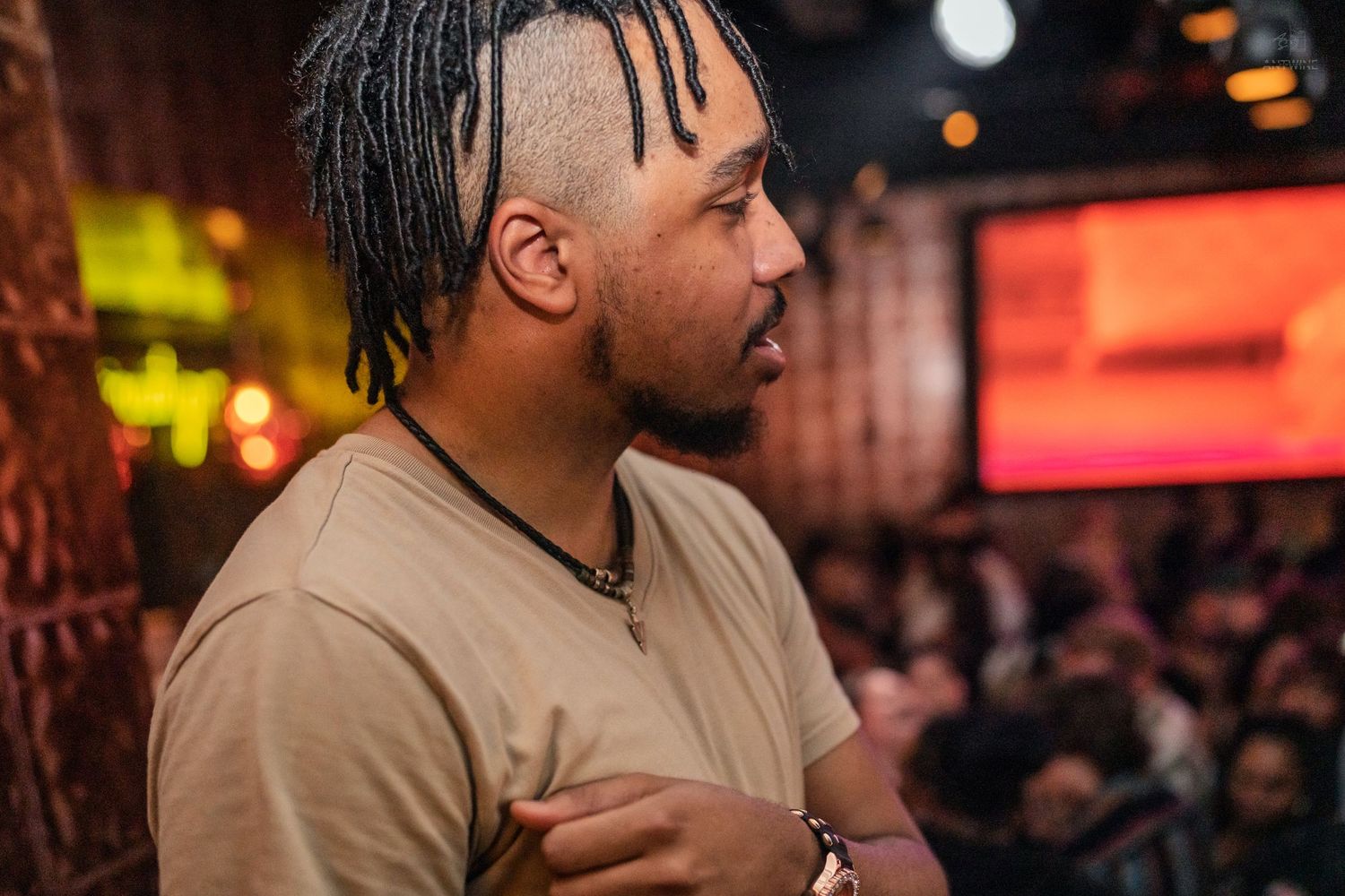 Young man with braided hair in a beige shirt at a nightclub event.