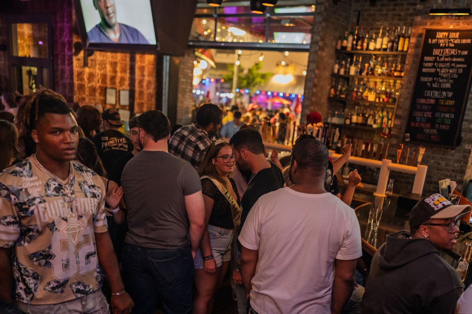 Busy bar interior with diverse crowd of people mingling and socializing under warm lighting at a lively nightclub event.