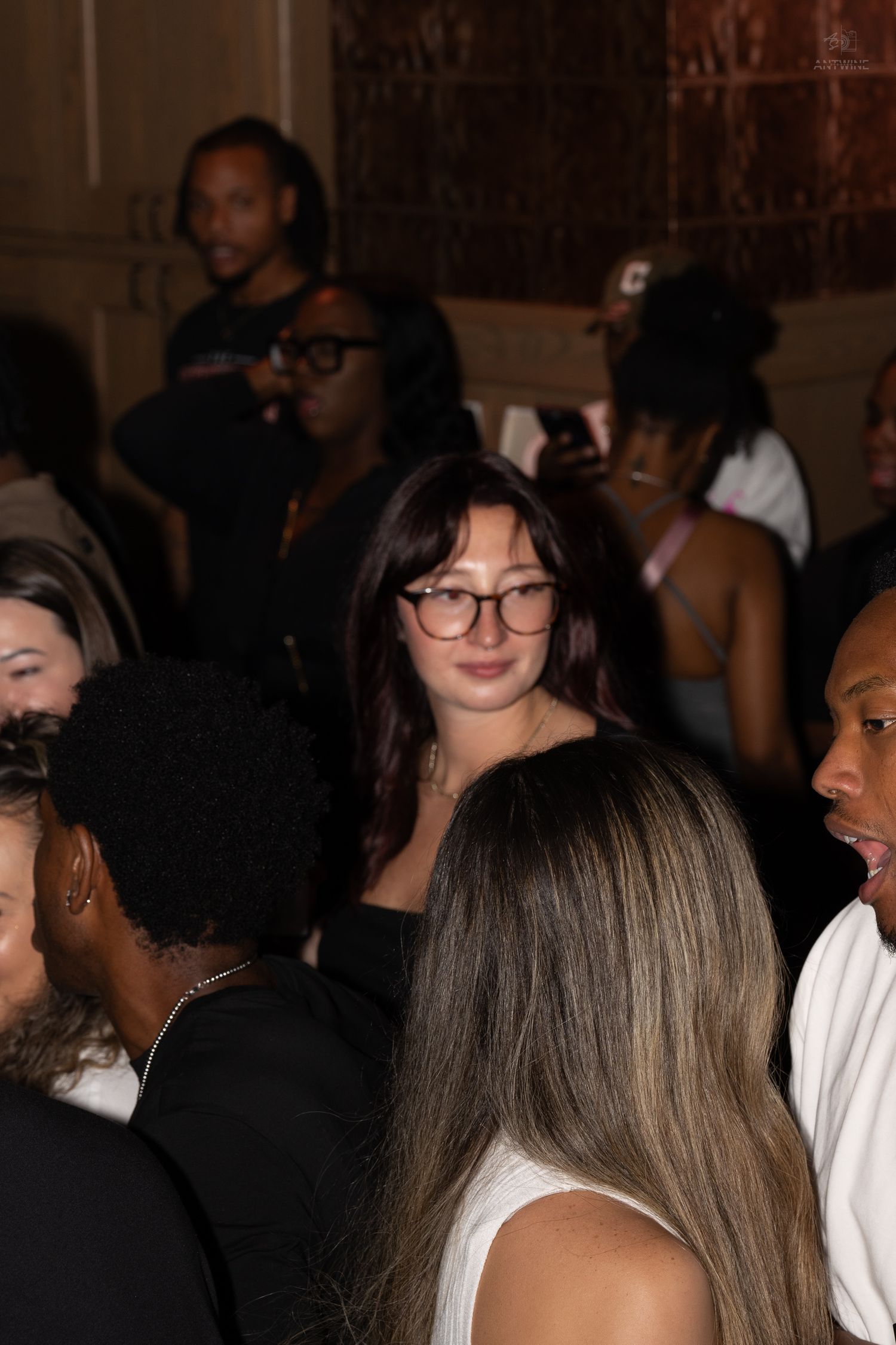 Young woman with glasses and dark hair standing in a crowded nightclub event.