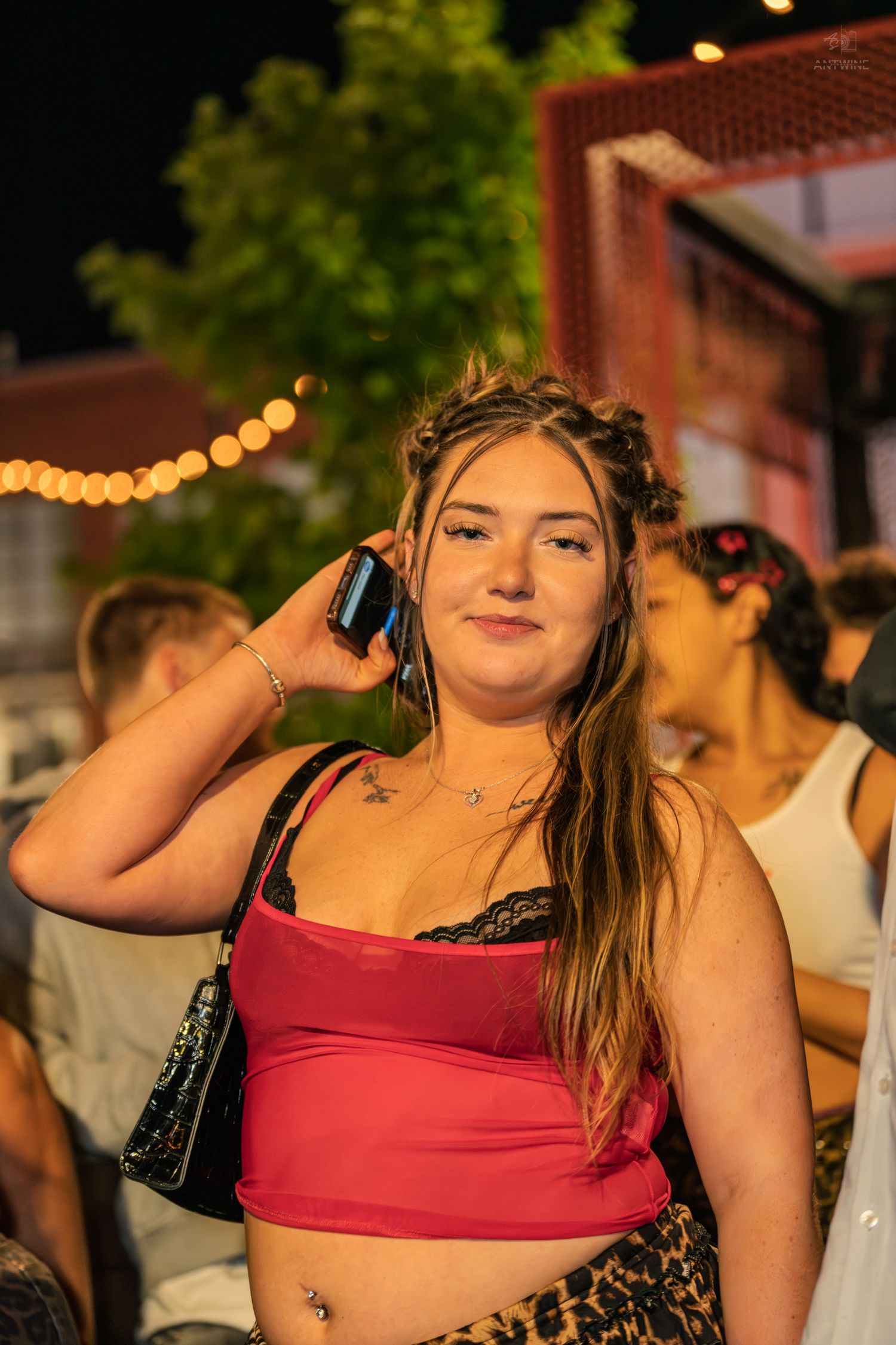 Young woman in red crop top posing with phone at an outdoor evening social gathering.