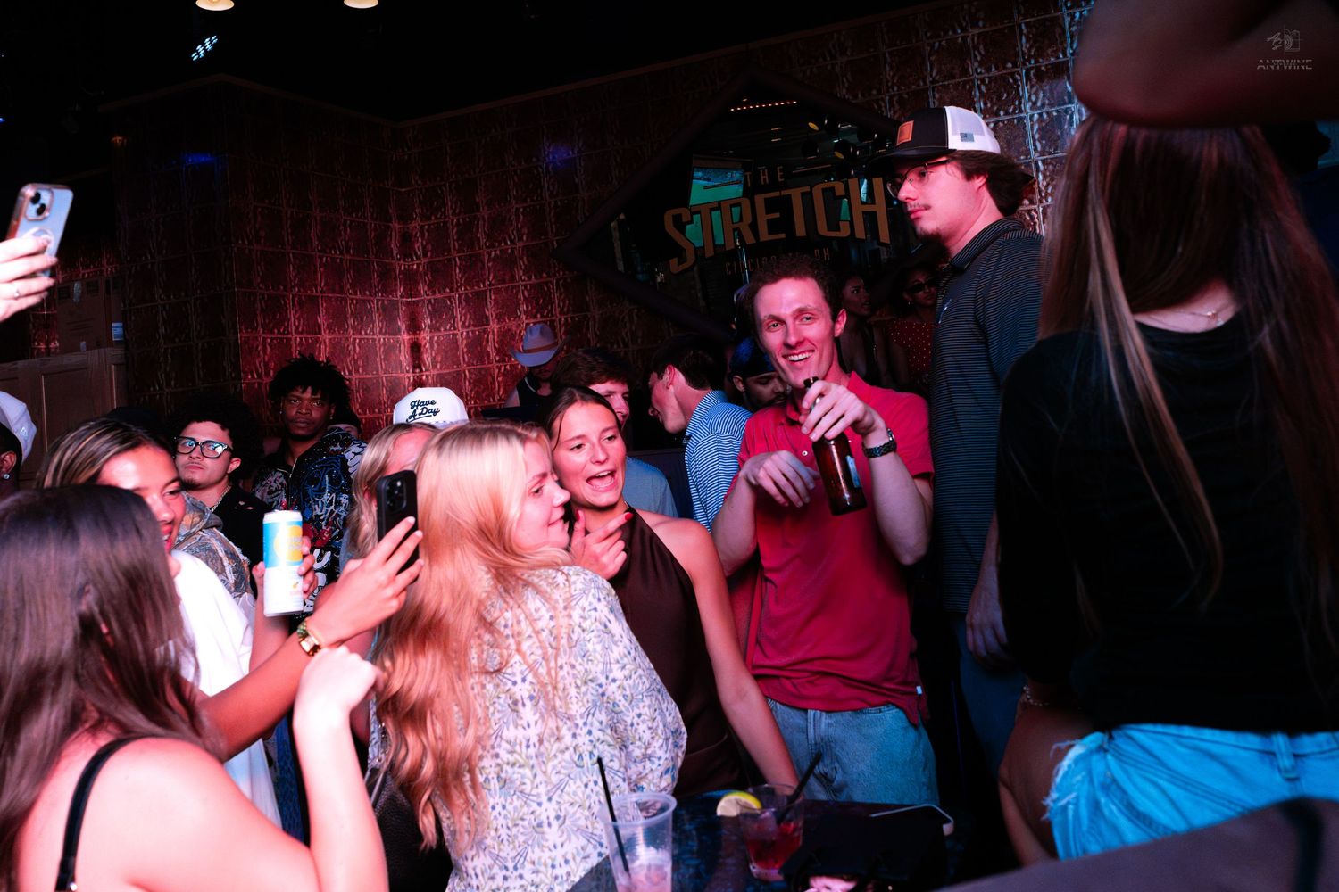 Excited crowd celebrating at a lively bar with neon sign backdrop.