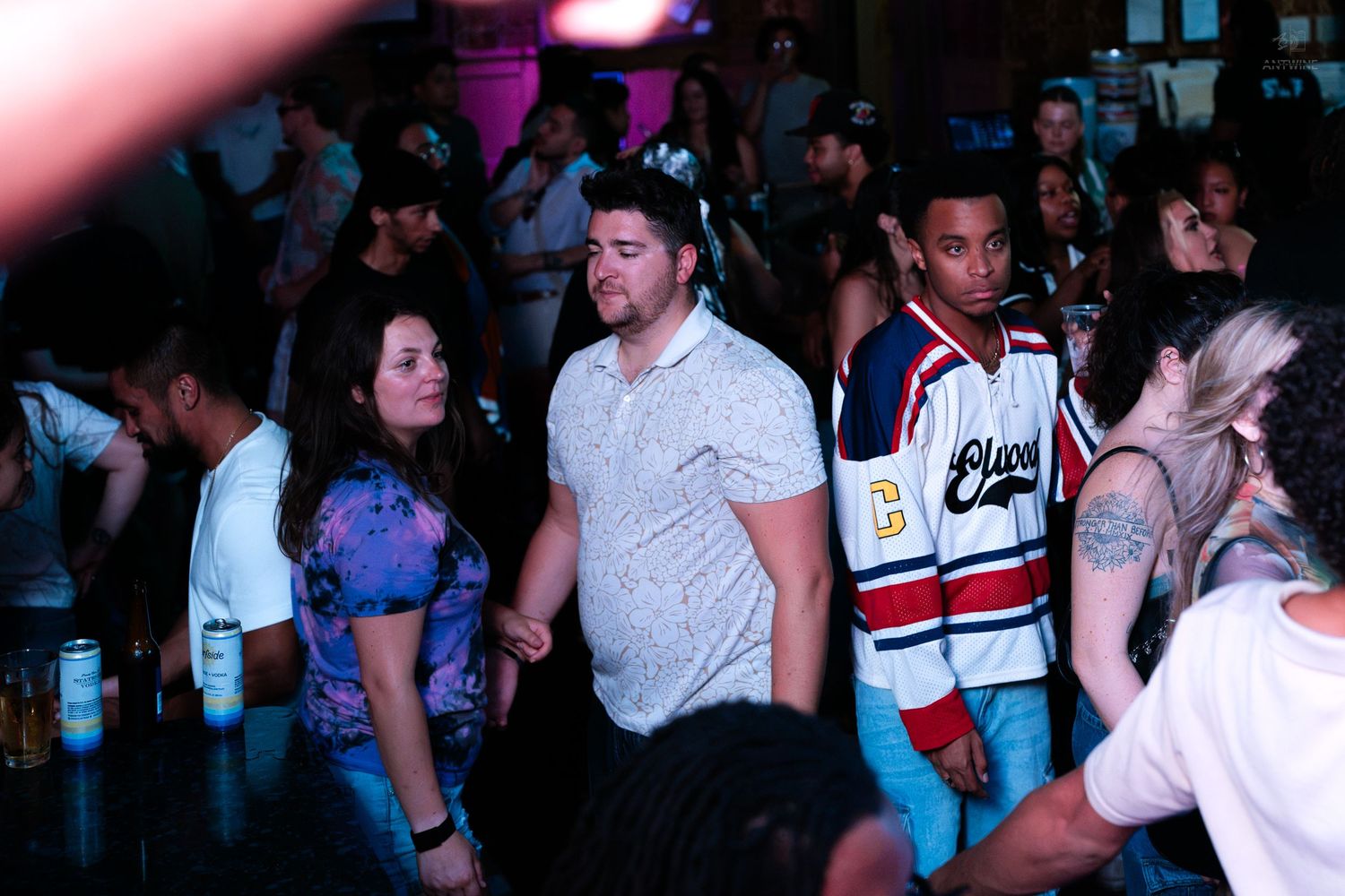 Group of young adults dancing together on a crowded nightclub dance floor.