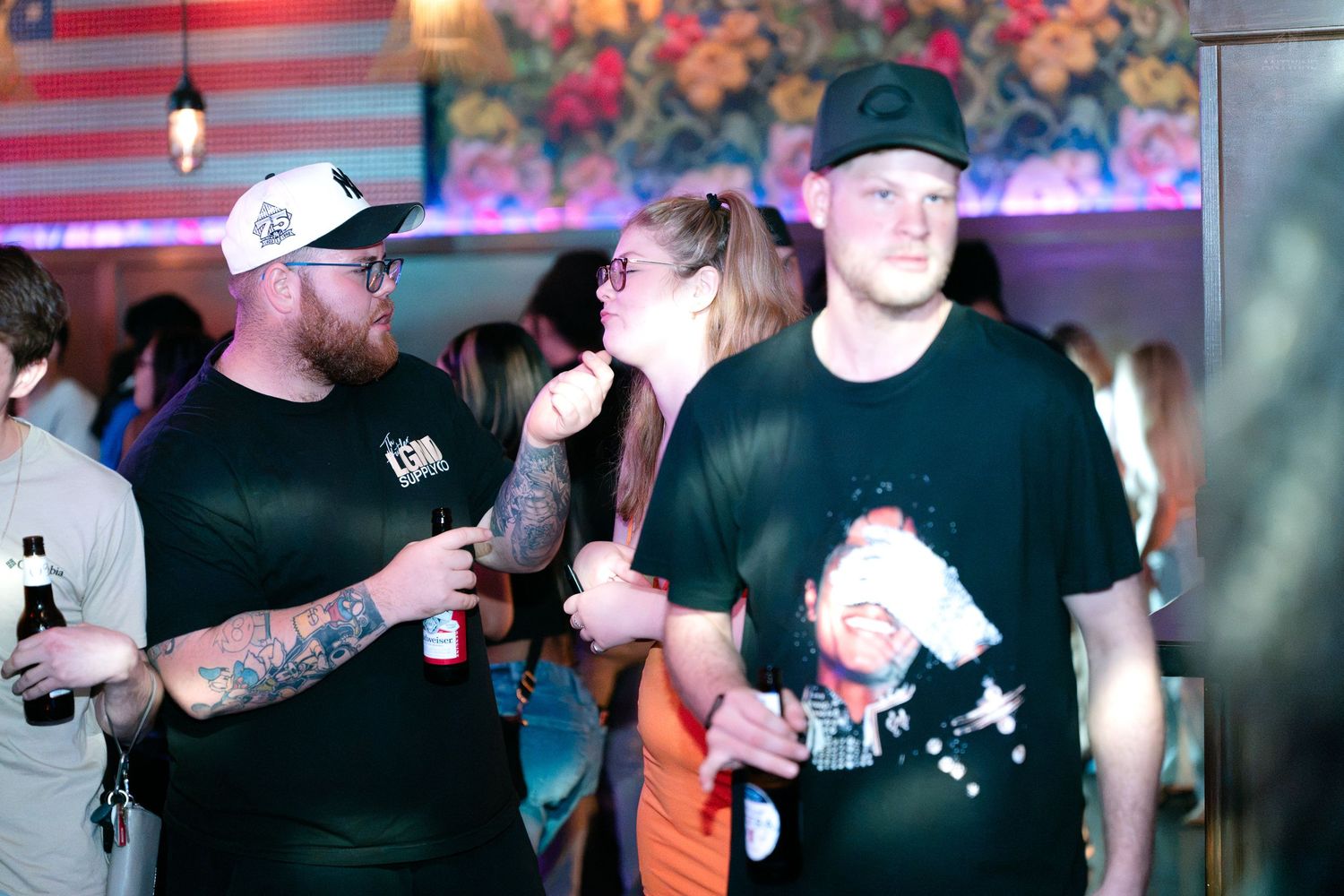 Two tattooed men holding drinks and chatting at a casual nightclub social event.