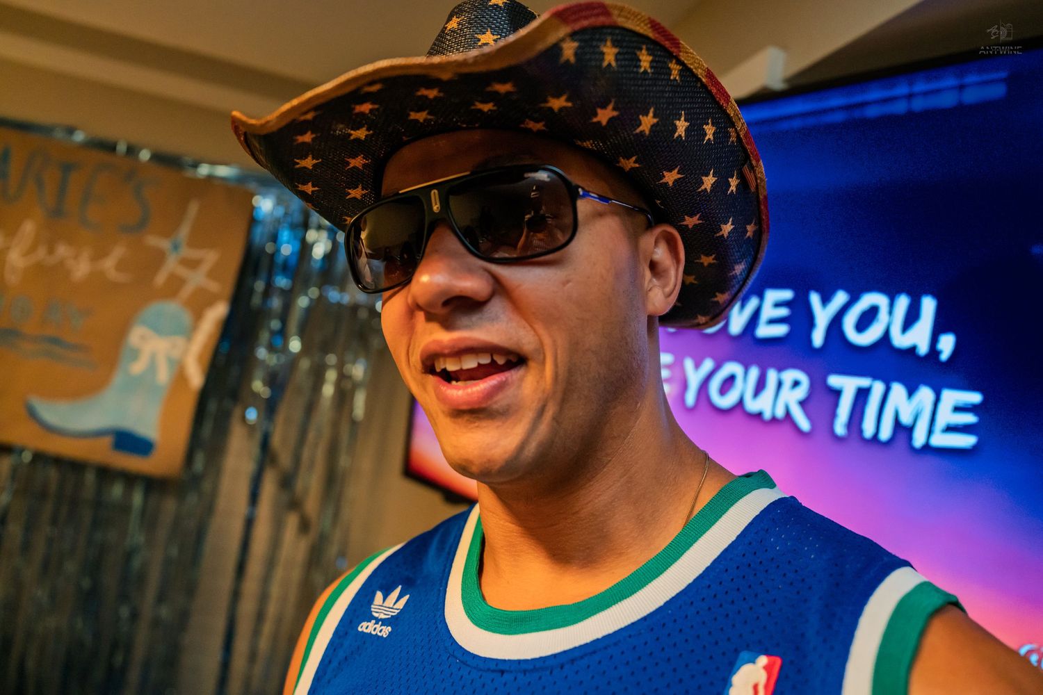 Smiling man in a star cowboy hat and Celtics jersey at a festive indoor birthday party.