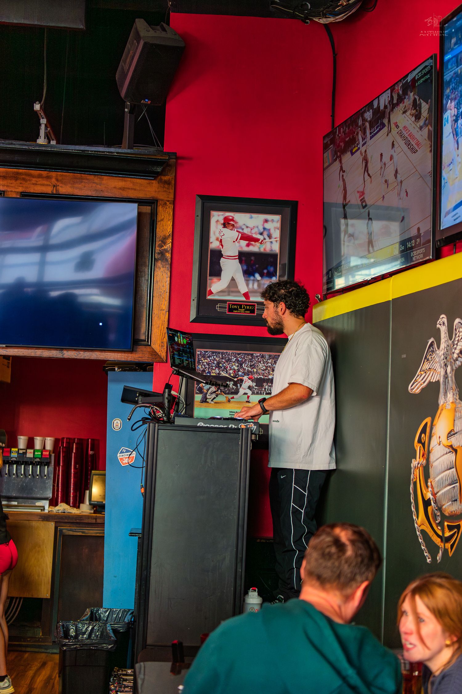 Man working at a bar POS terminal surrounded by sports memorabilia and TVs in a vibrant red sports bar.