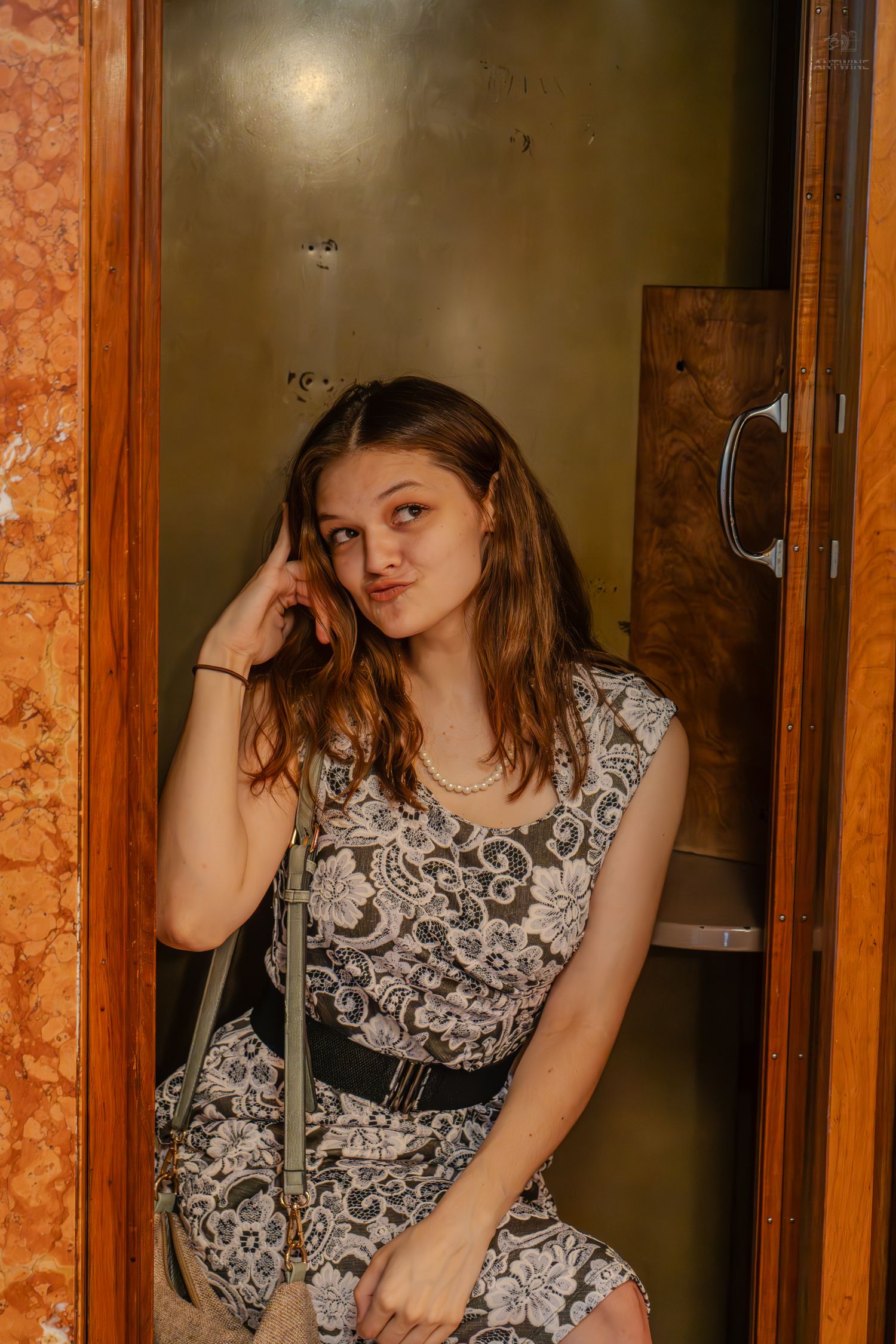 Young woman in floral dress sitting in elevator, holding phone to ear with thoughtful expression.