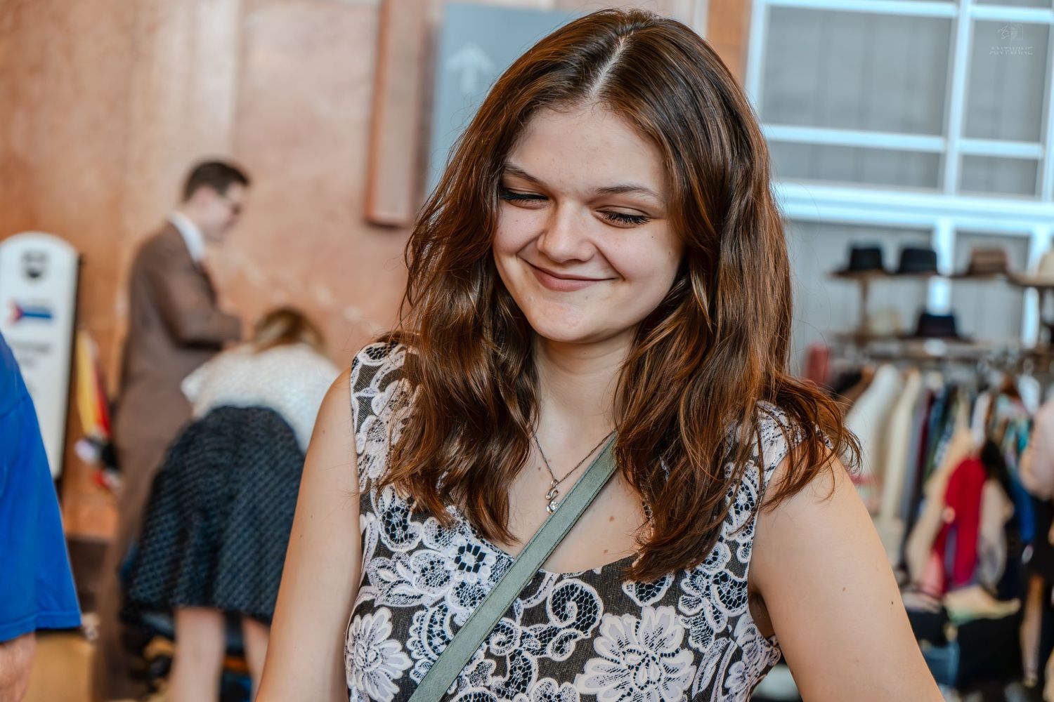 Young woman smiling while browsing clothing at a boutique fashion store, wearing a floral sleeveless top.