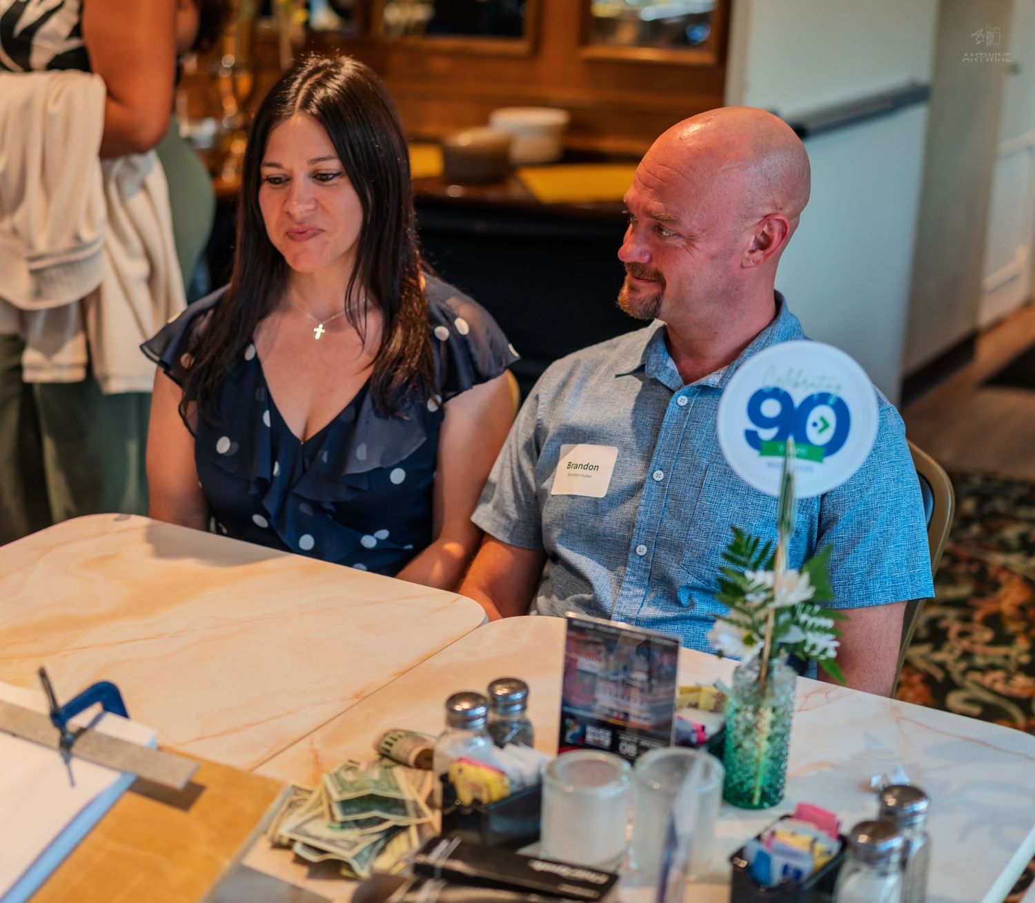 A bald man and dark-haired woman sit together at a table during a social event, smiling and relaxed.