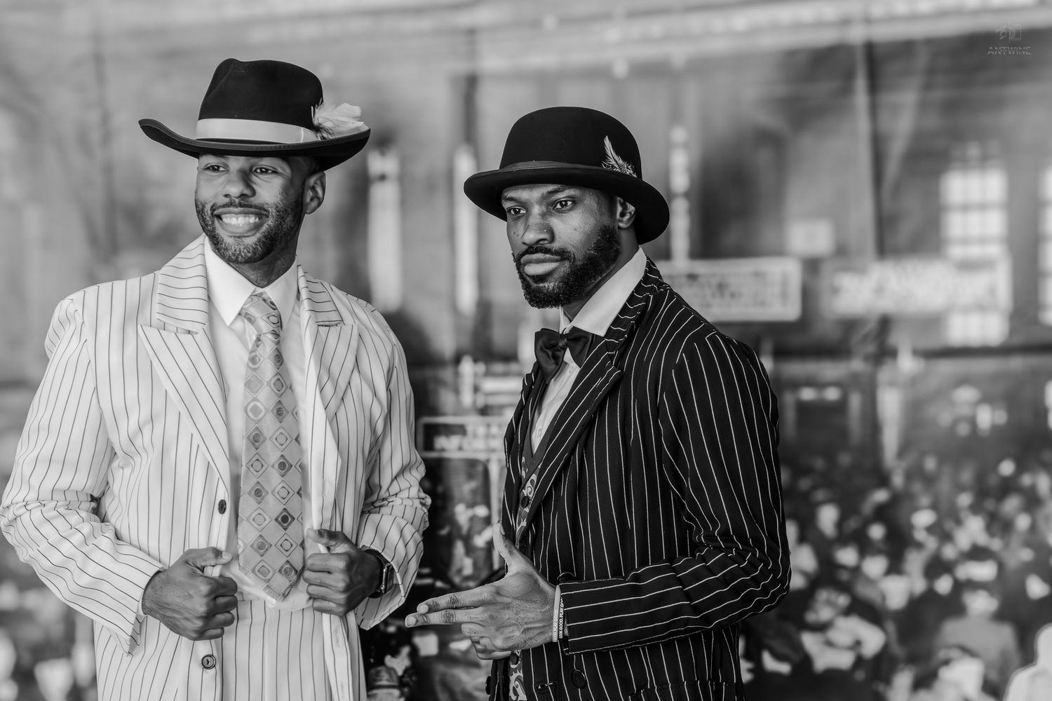 Two men in vintage pinstripe zoot suits and fedora hats pose in a classic black and white portrait photo.