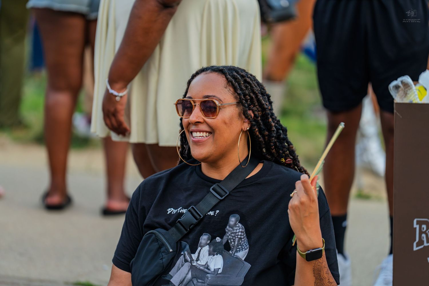 Smiling woman with locs and sunglasses holding a drumstick at an outdoor Juneteenth celebration.