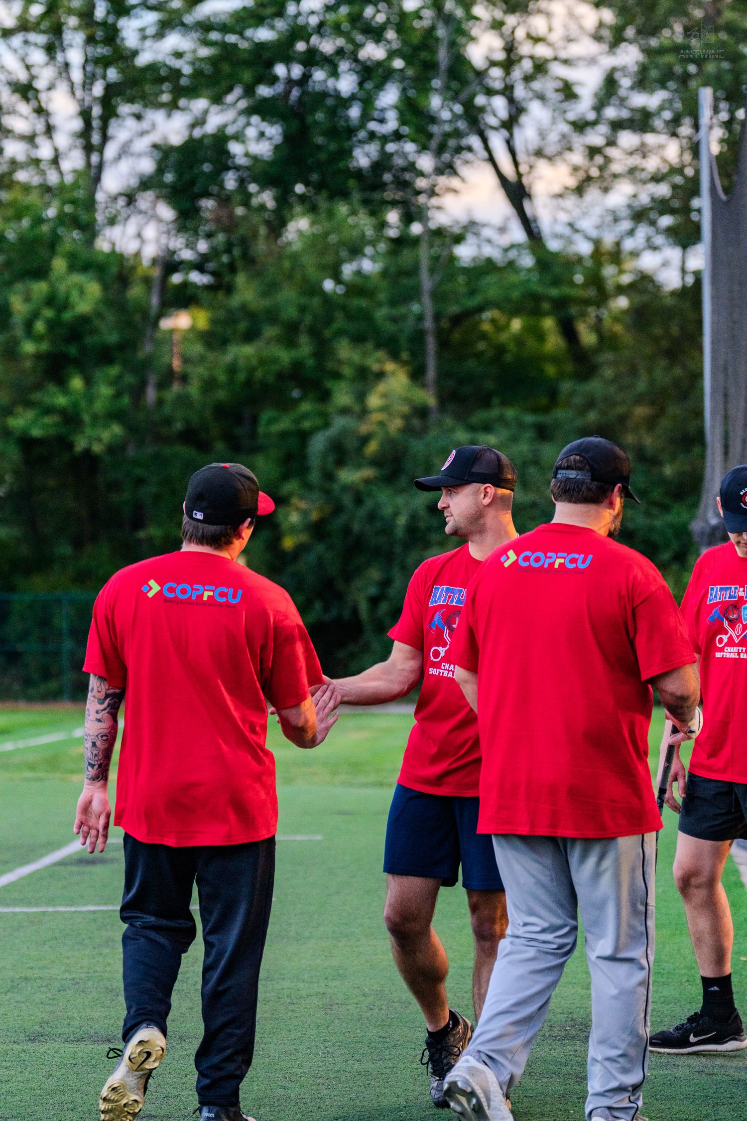 Team members in red COPFCU shirts shake hands walking off softball field after game.