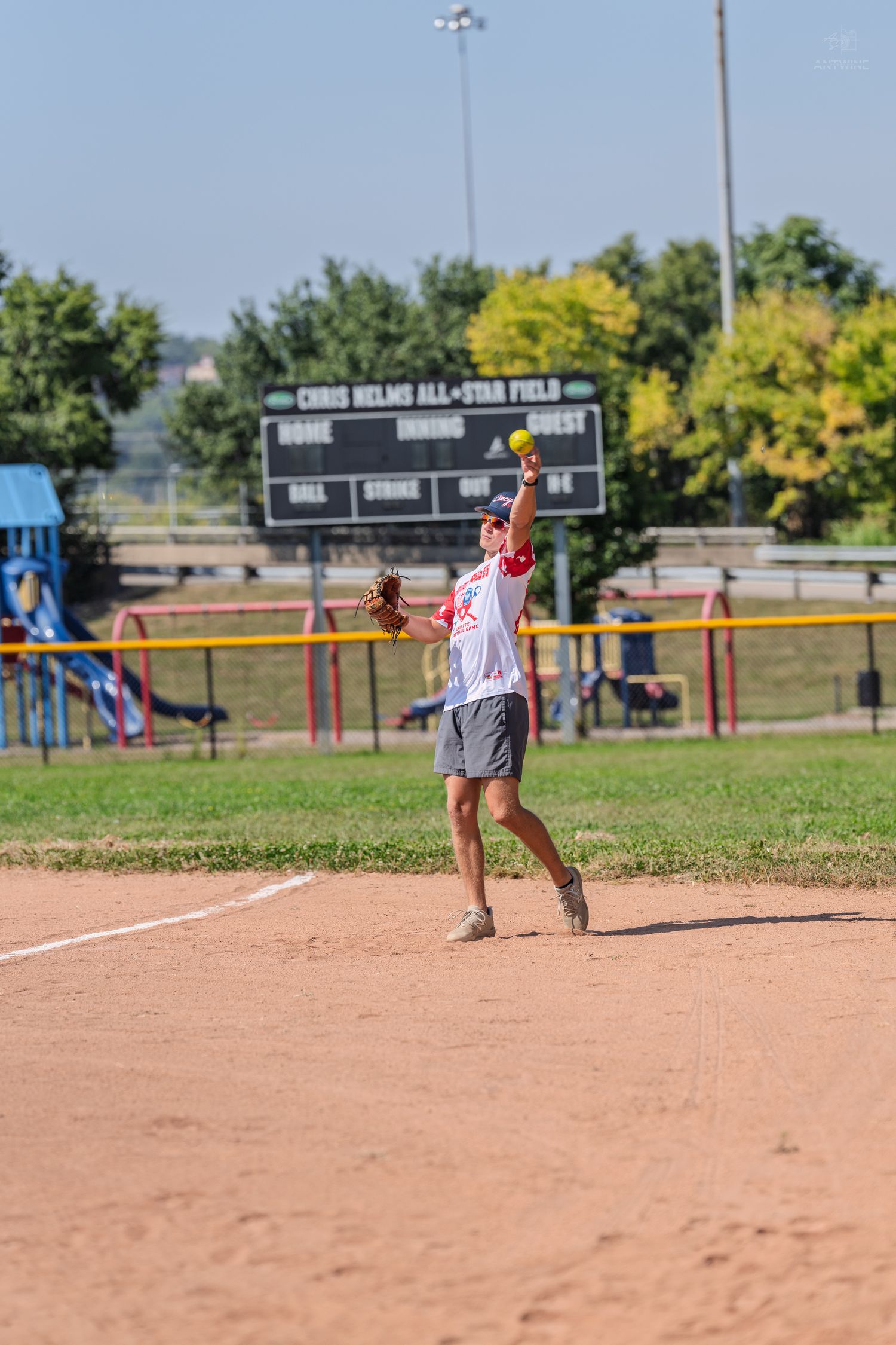 A softball pitcher winds up to throw during a game at Chris Helms All-Star Field on a bright sunny day.