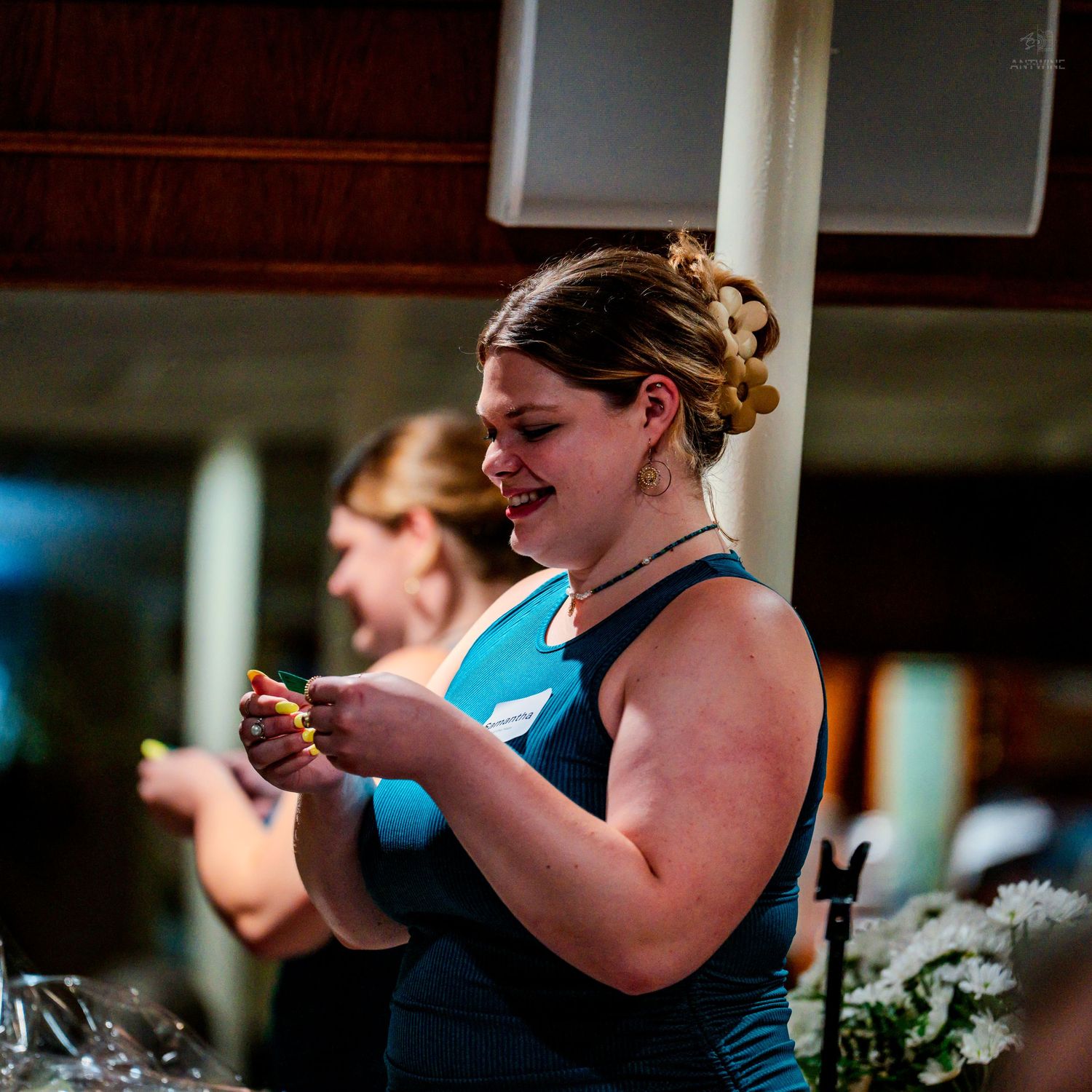 A smiling woman in a teal dress holds an item at an indoor social gathering or banquet event.
