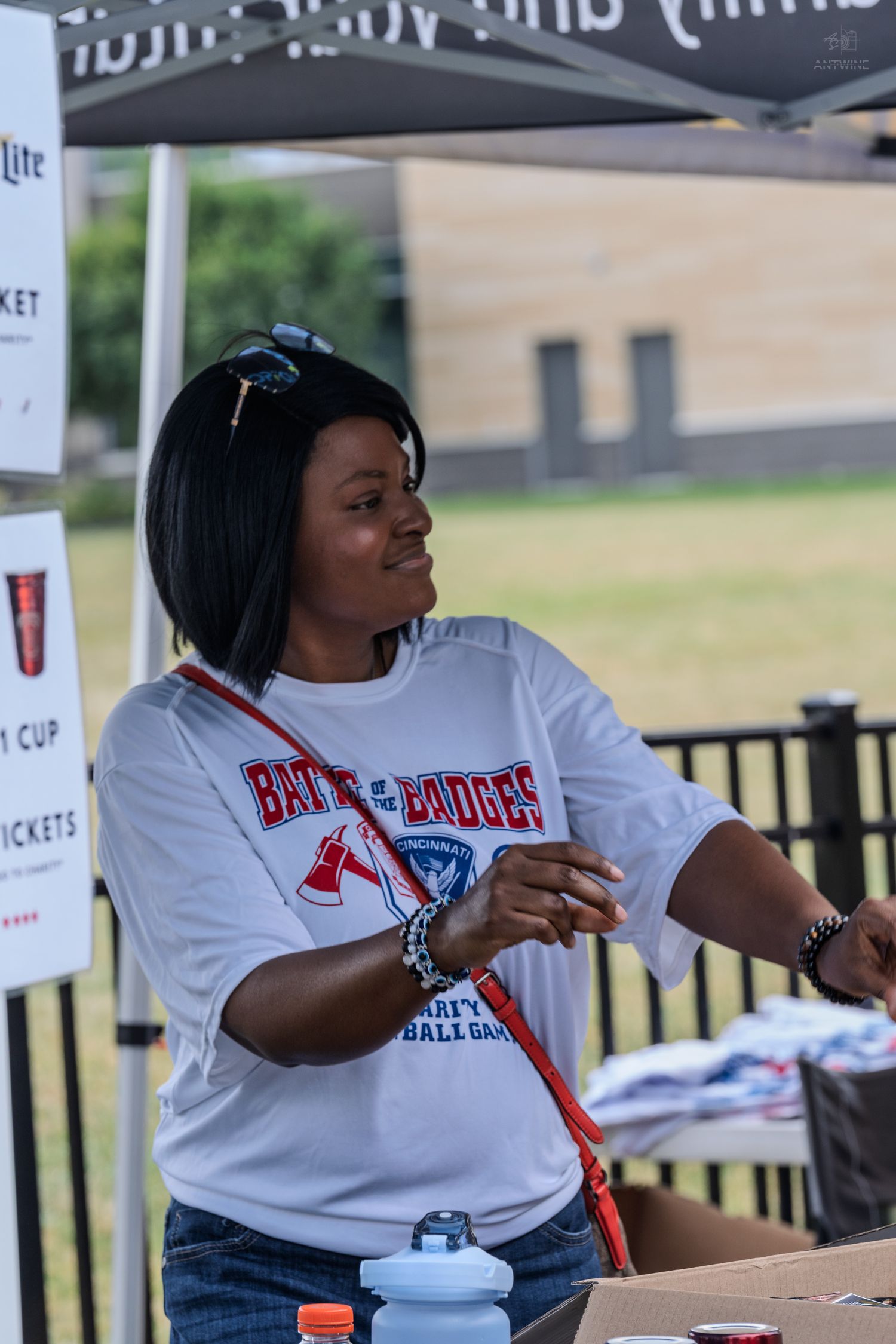 A woman in a Battle of Badges charity softball game shirt works at an outdoor event booth.