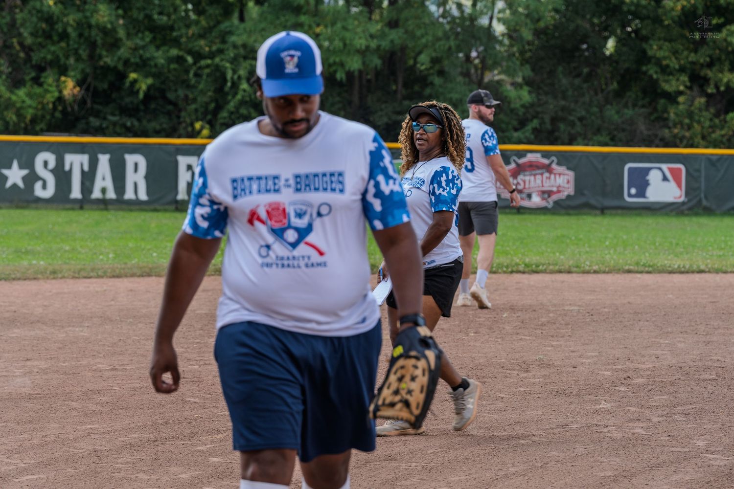Athletes in Battle of the Badges charity softball game uniforms walking across baseball diamond field.