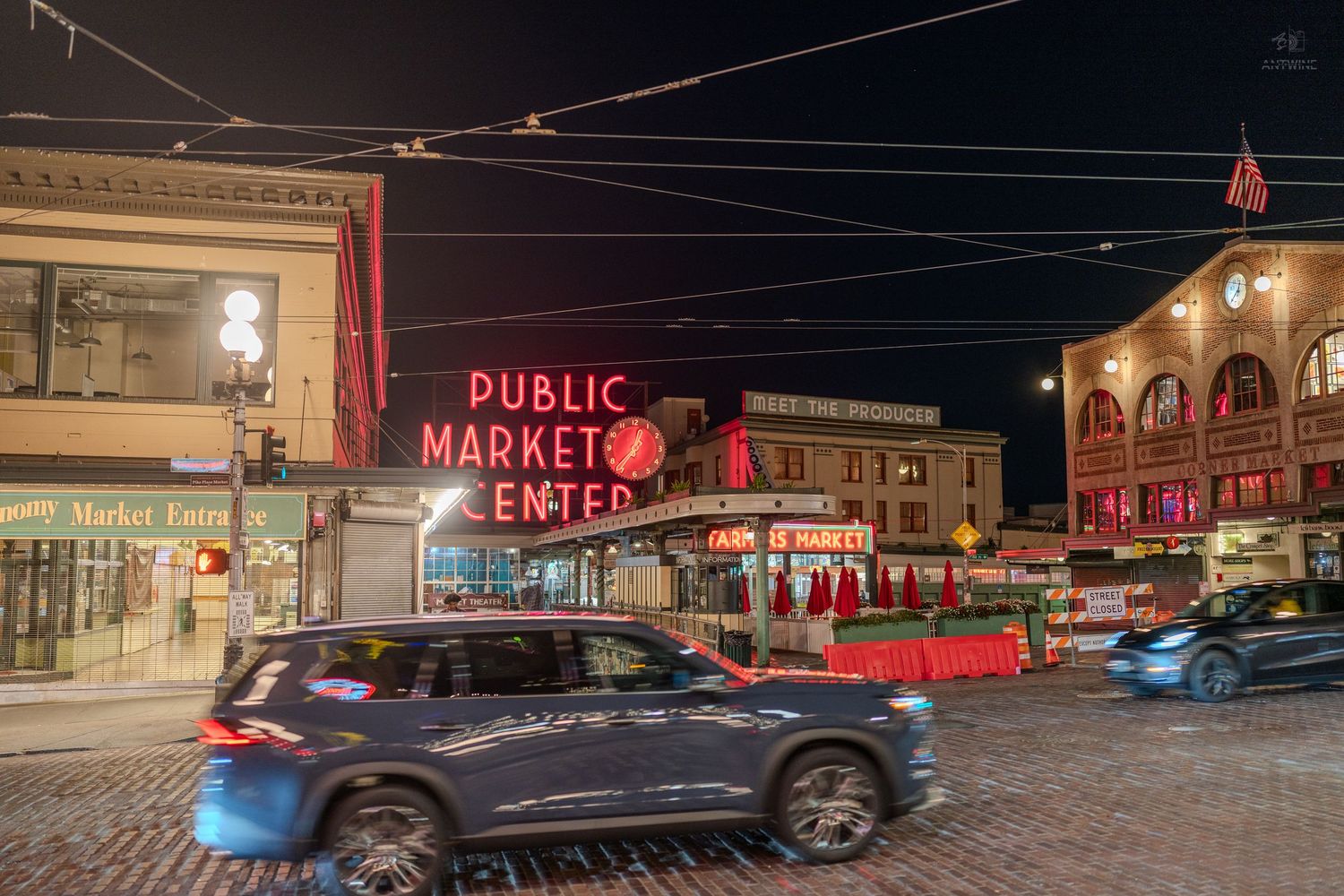 Pike Place Public Market Center neon sign with traffic and brick buildings at night.