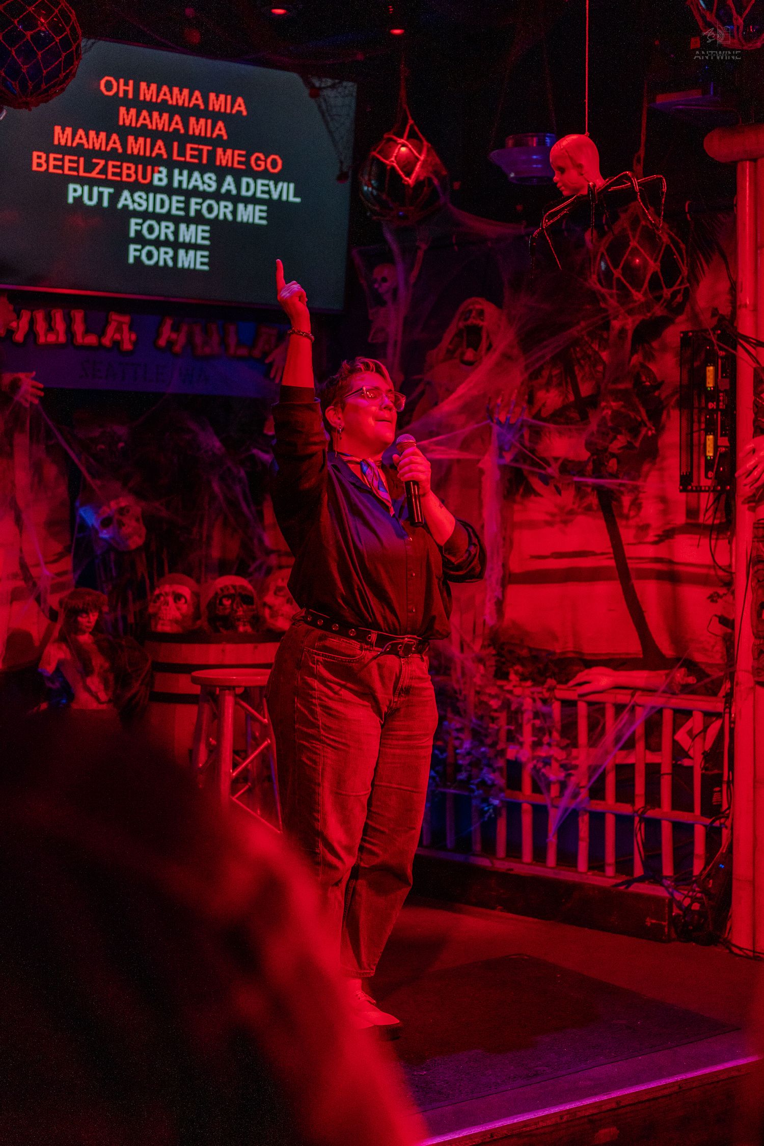 Singer performing Bohemian Rhapsody at a Halloween-themed karaoke bar under red stage lighting.