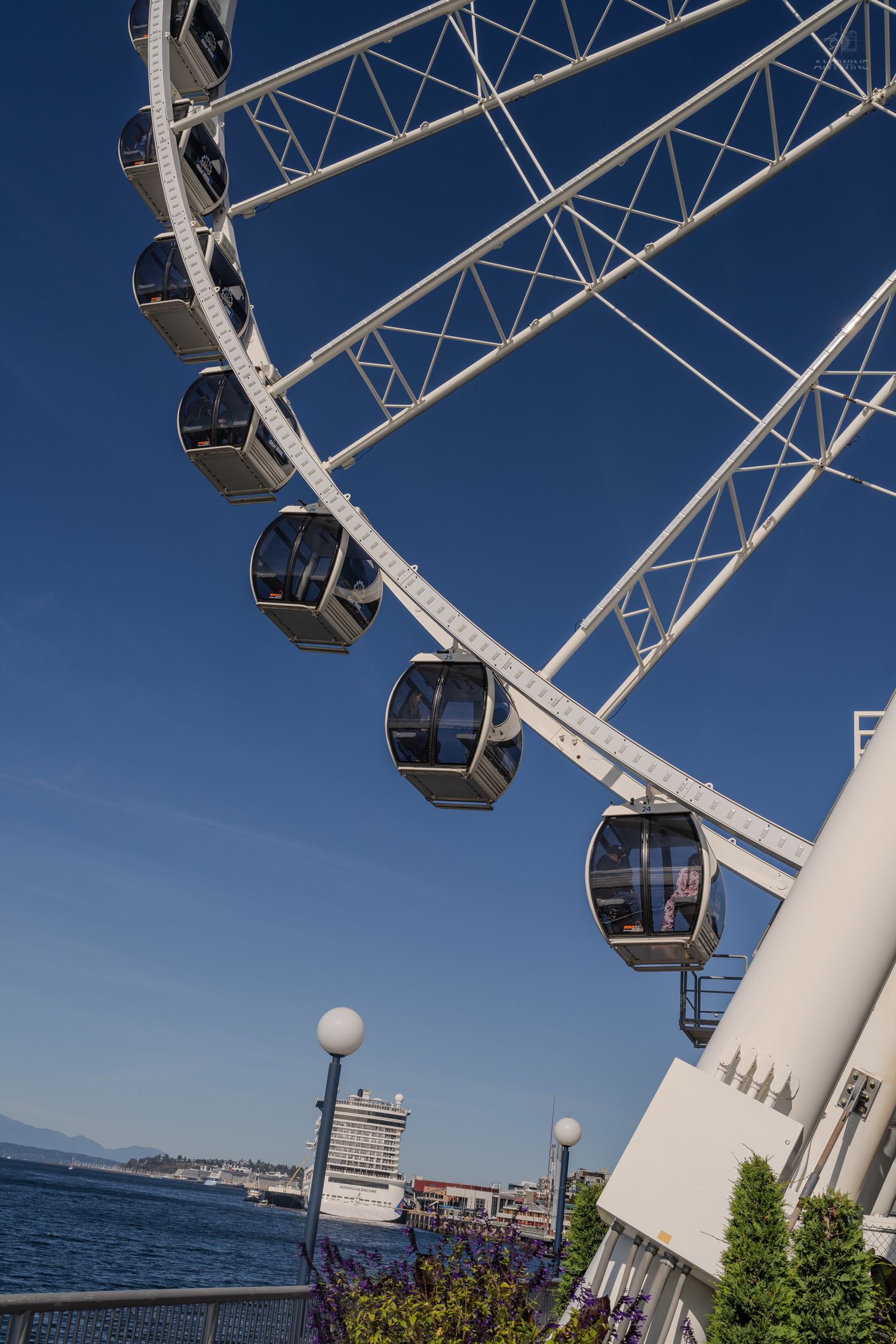 Close-up of Seattle Great Wheel gondola cabins against clear blue sky with cruise ship and Puget Sound visible.