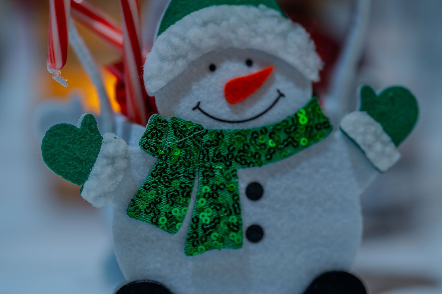 A cheerful white snowman decoration with a green sequin scarf, mittens, and candy cane accents for Christmas.