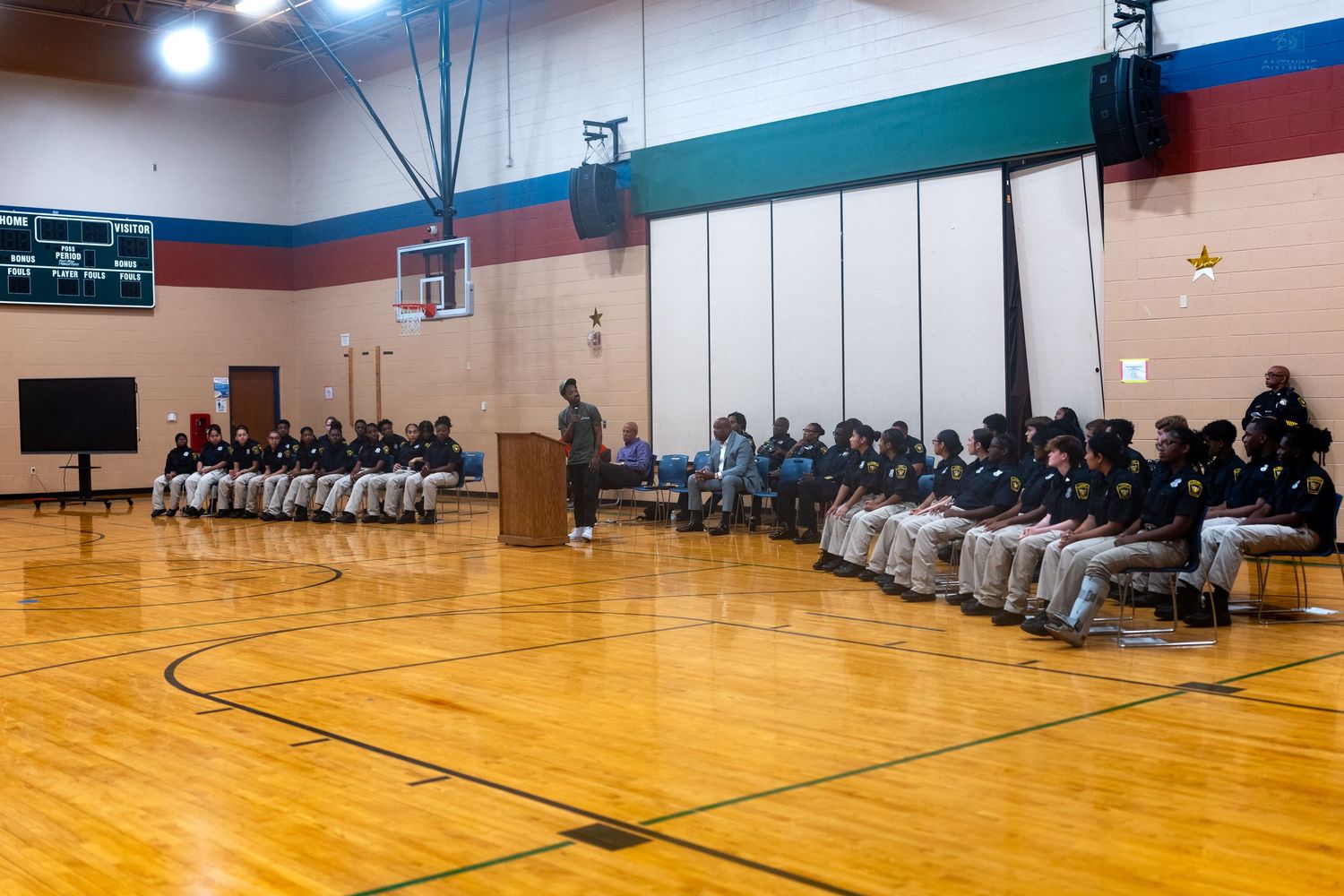 Students and staff gathered in a school gymnasium for a formal assembly ceremony on a hardwood basketball court.