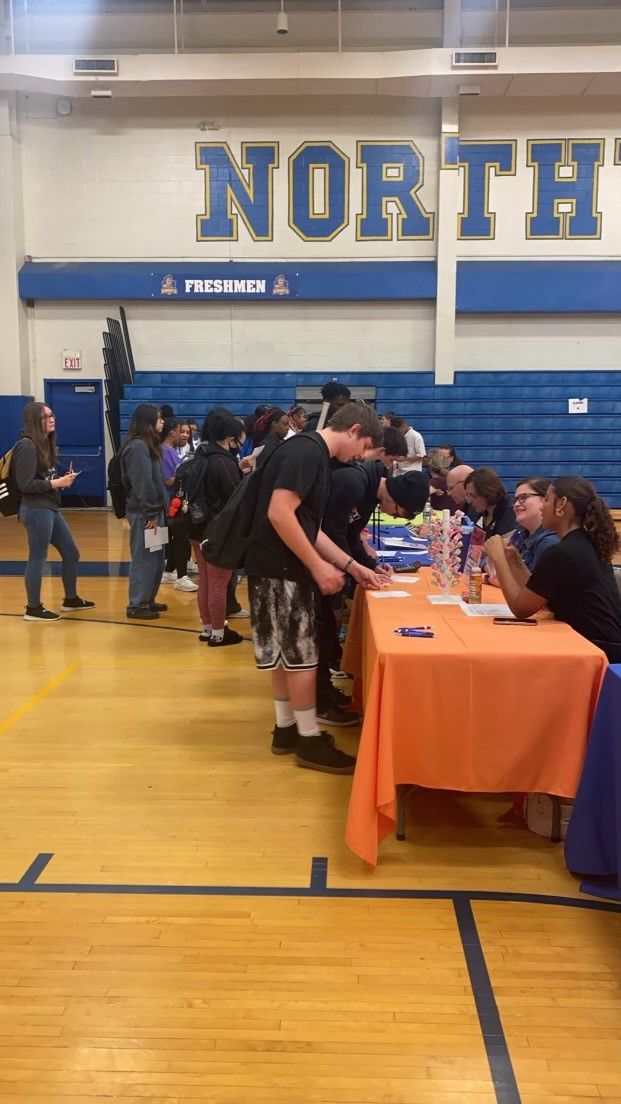 Students line up at tables in a school gymnasium during a Northtown High School freshmen orientation event.