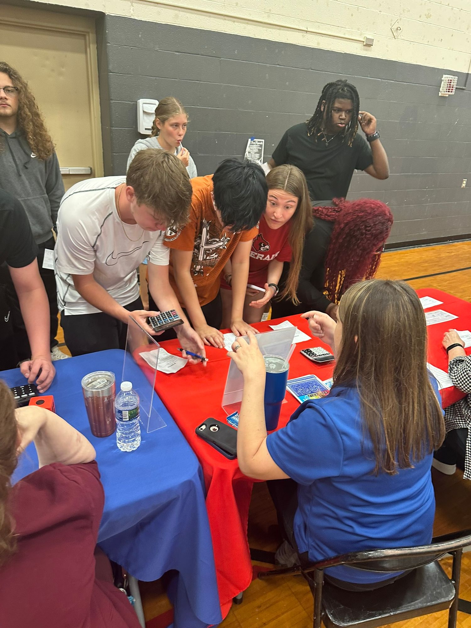 High school students interact with a representative at a red table during a school career fair.