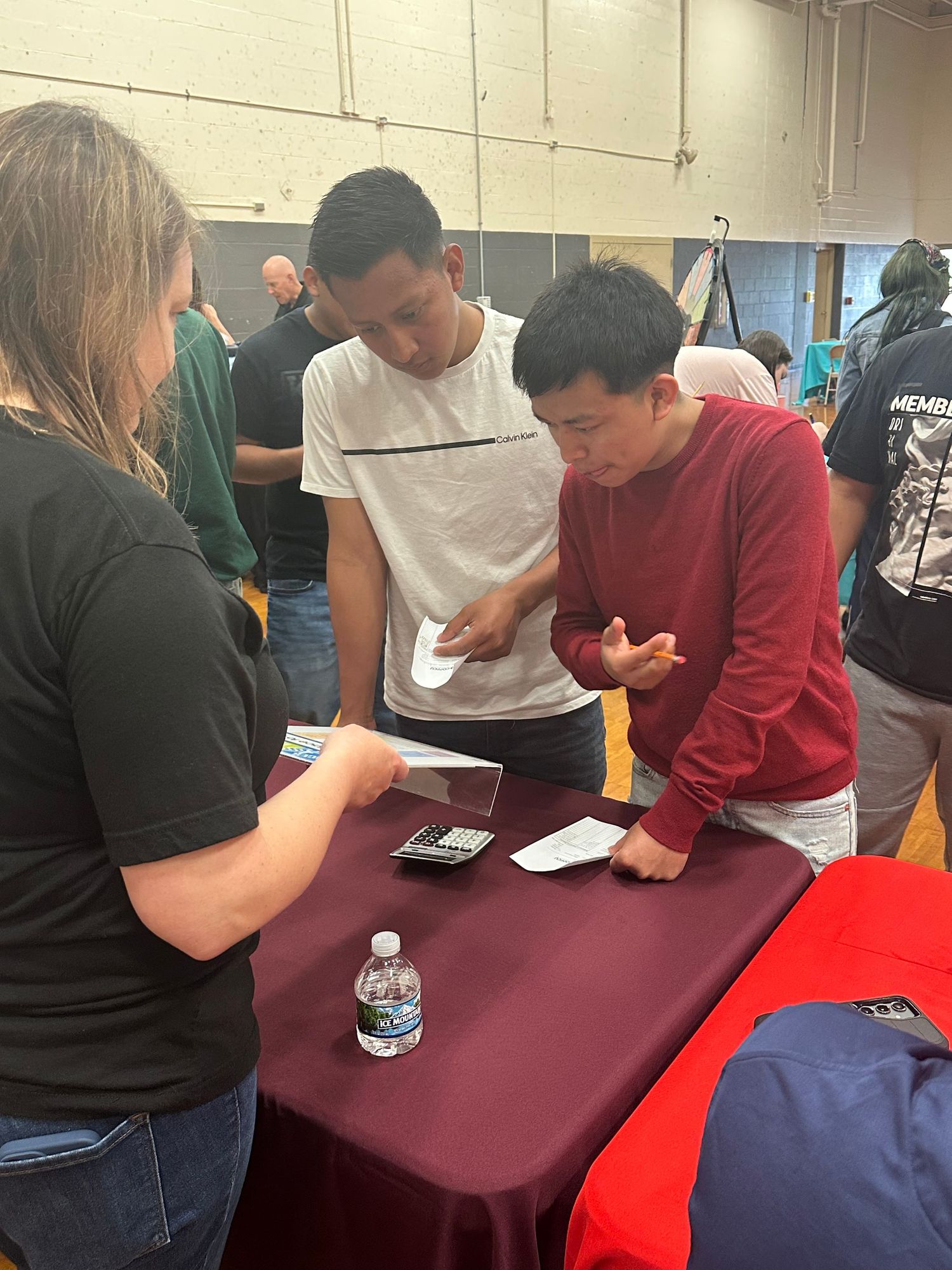 Students gather around a table at a school fair event, reviewing papers and discussing information with a representative.