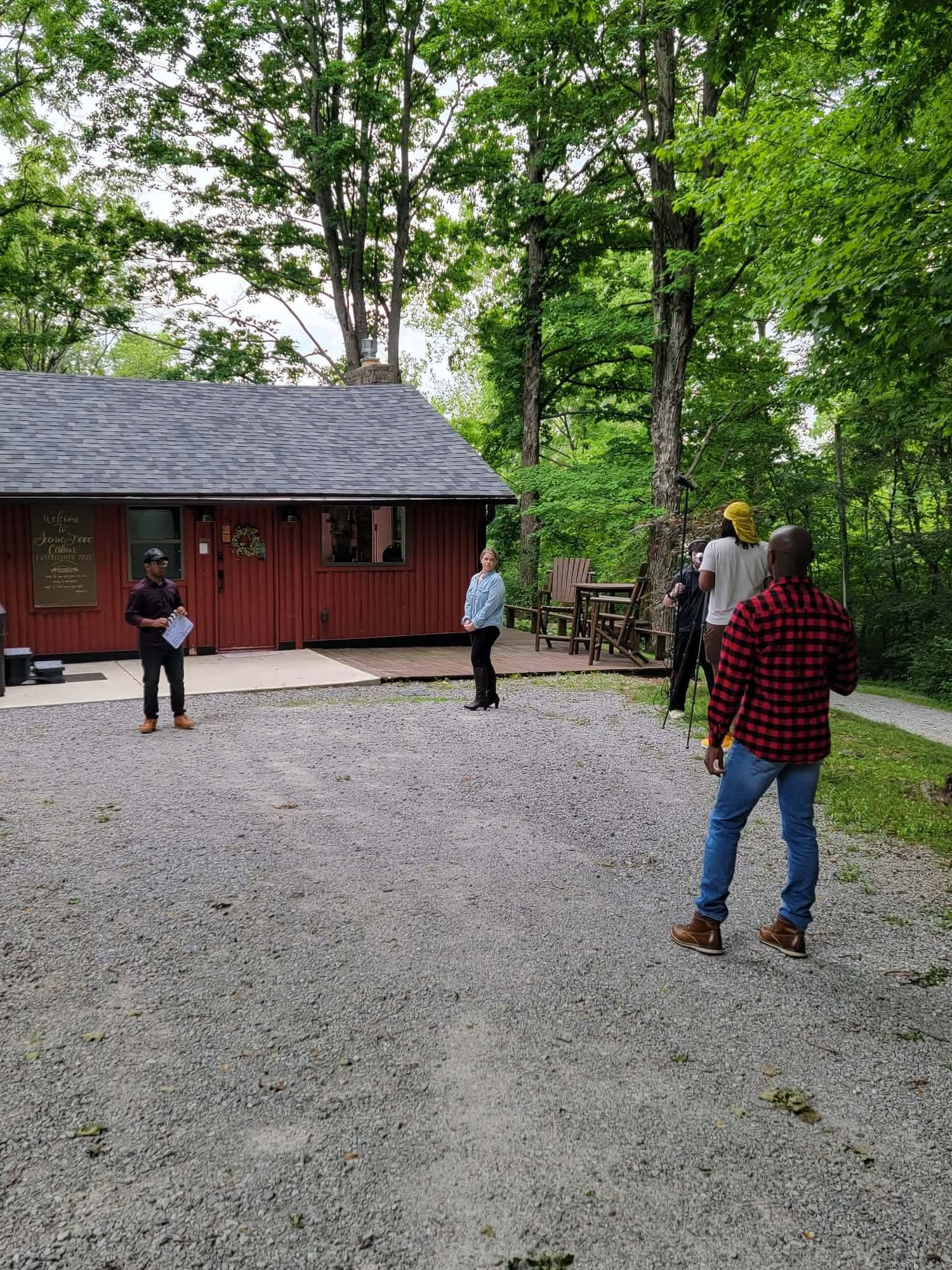 Film crew gathered outside red cabin in wooded area during production.