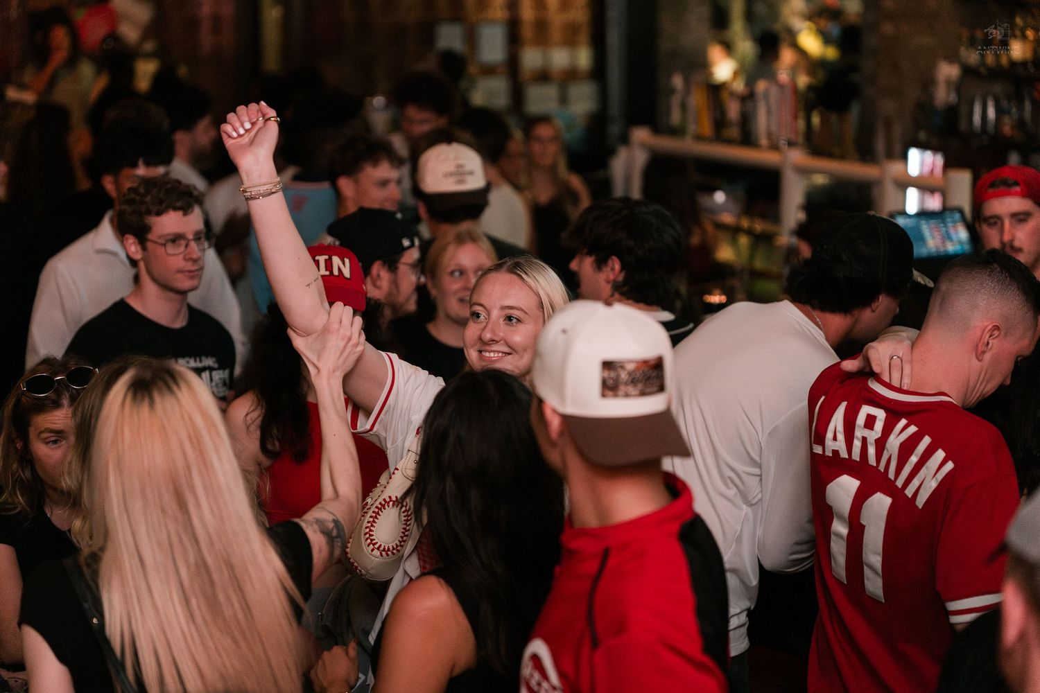 Crowd of young people celebrating at a lively bar, with a woman raising her fist in excitement.