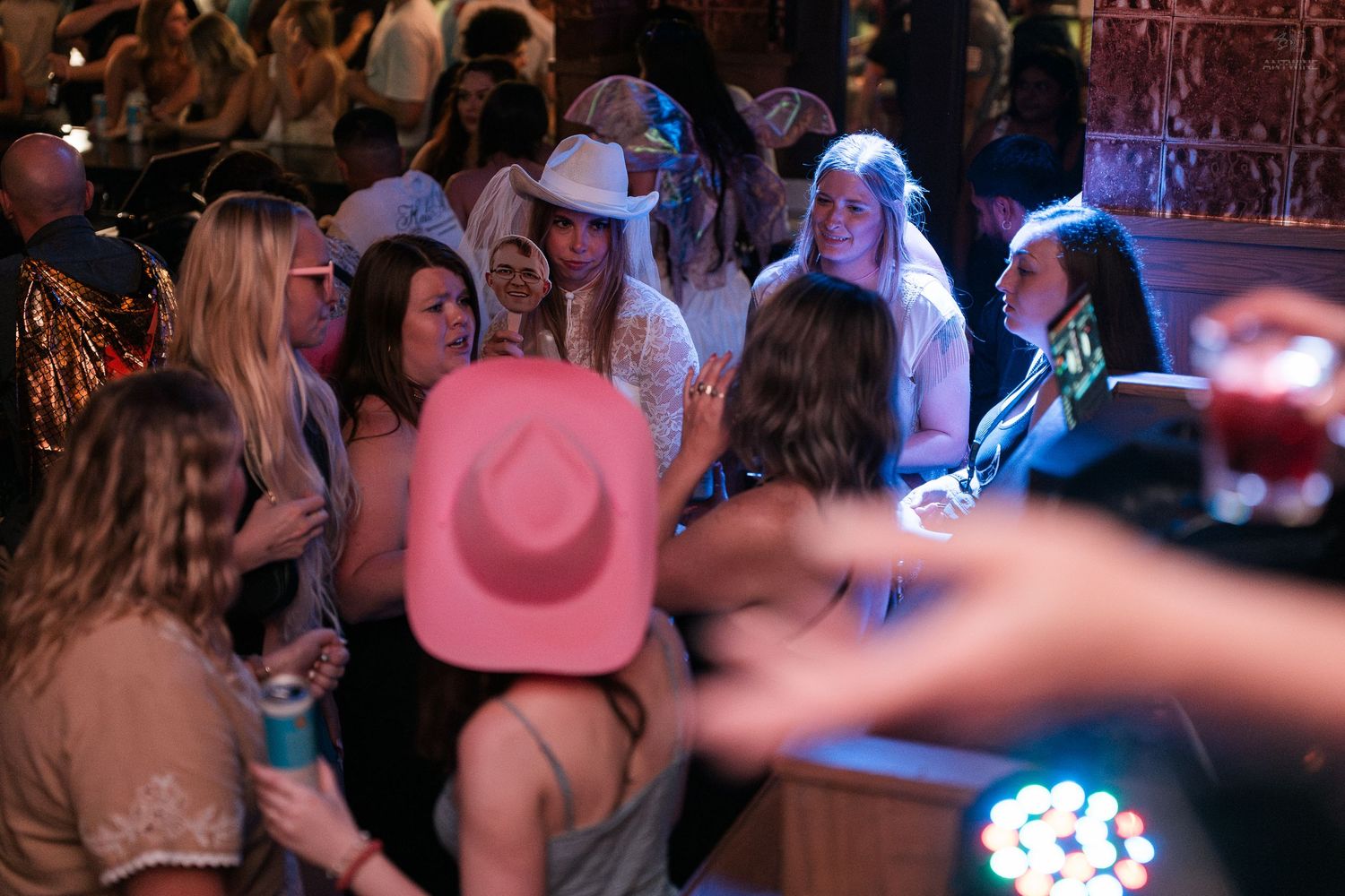 Group of women wearing cowboy hats gather together on a dance floor at a festive nightclub.