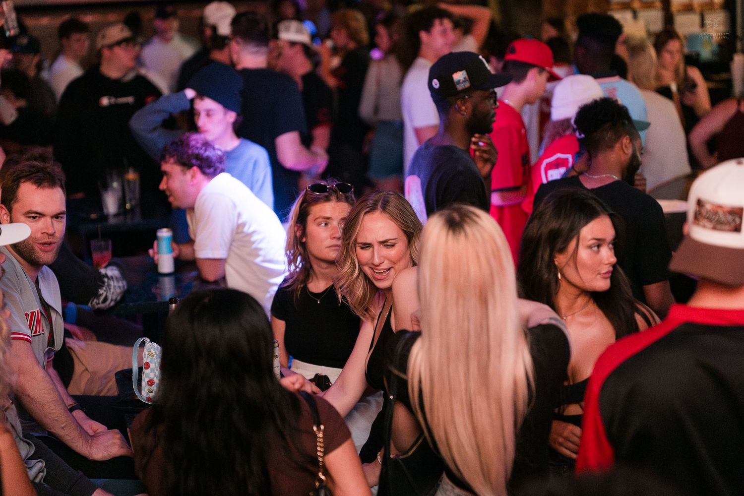 Group of young women socializing at a packed nightclub with dark ambient lighting.
