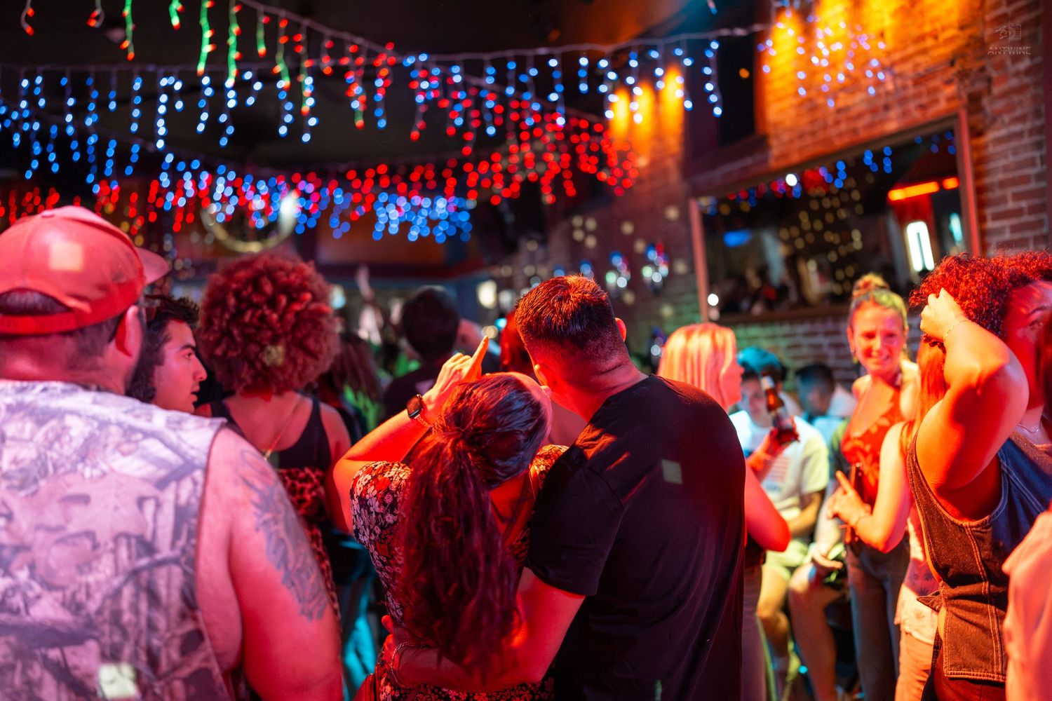 Colorful nightclub scene with people dancing under vibrant red and blue string lights in a lively bar.