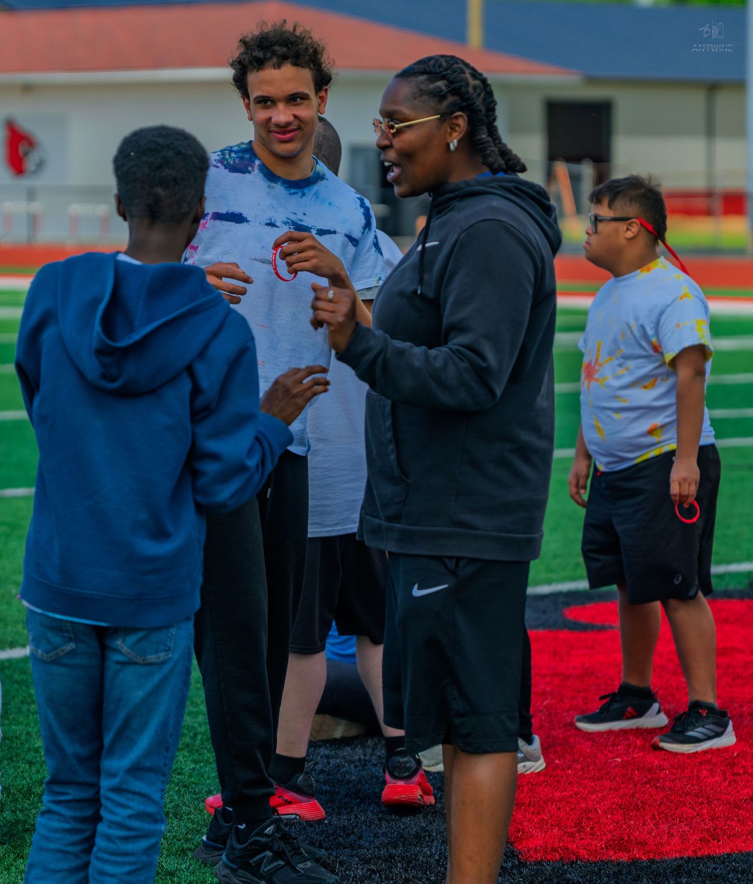 Group of youth and adults talking on a football field turf during an outdoor sports event or camp activity.