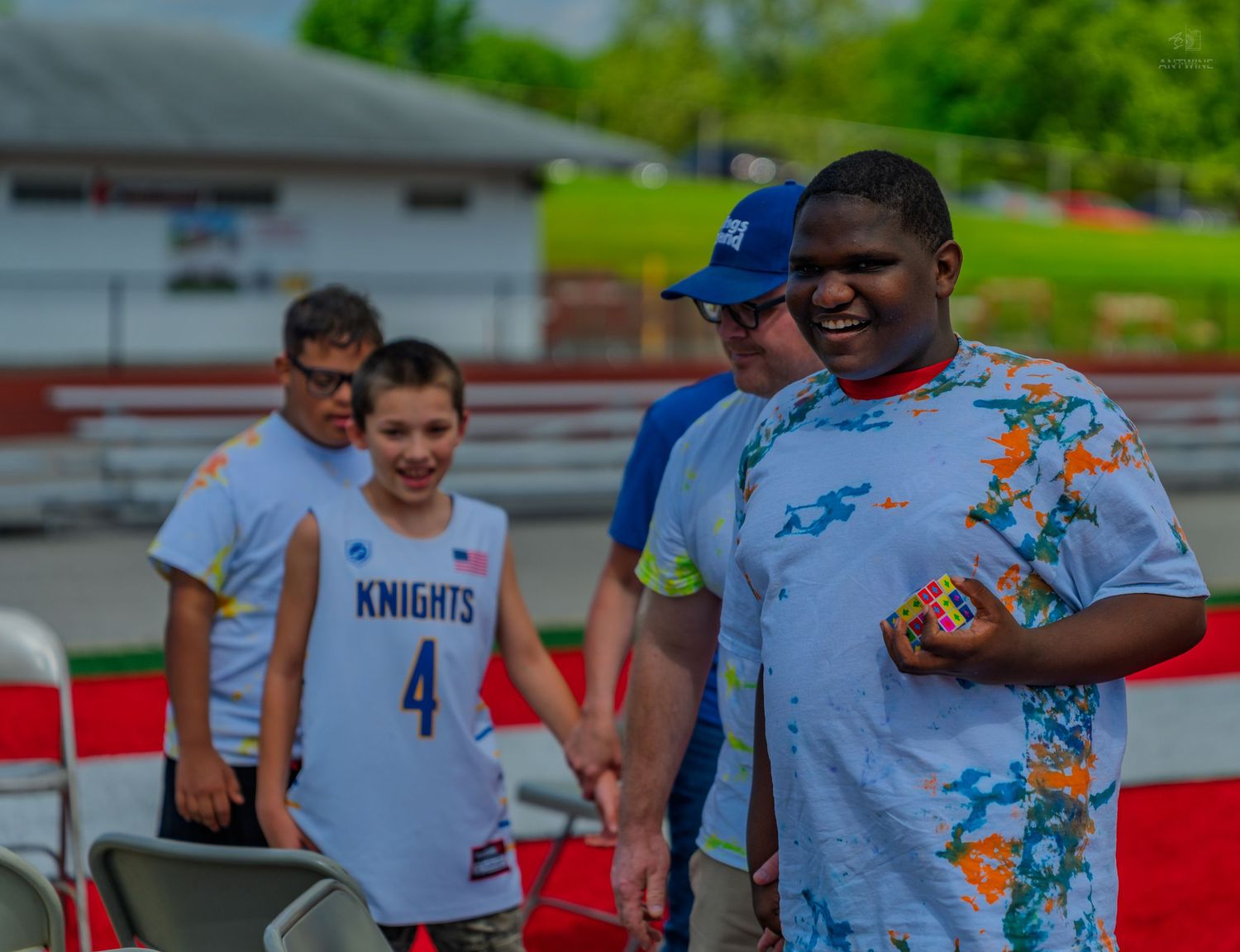 Youth athletes smile outdoors at a sports event, one wearing a Knights number 4 jersey, another holding a colorful cube.