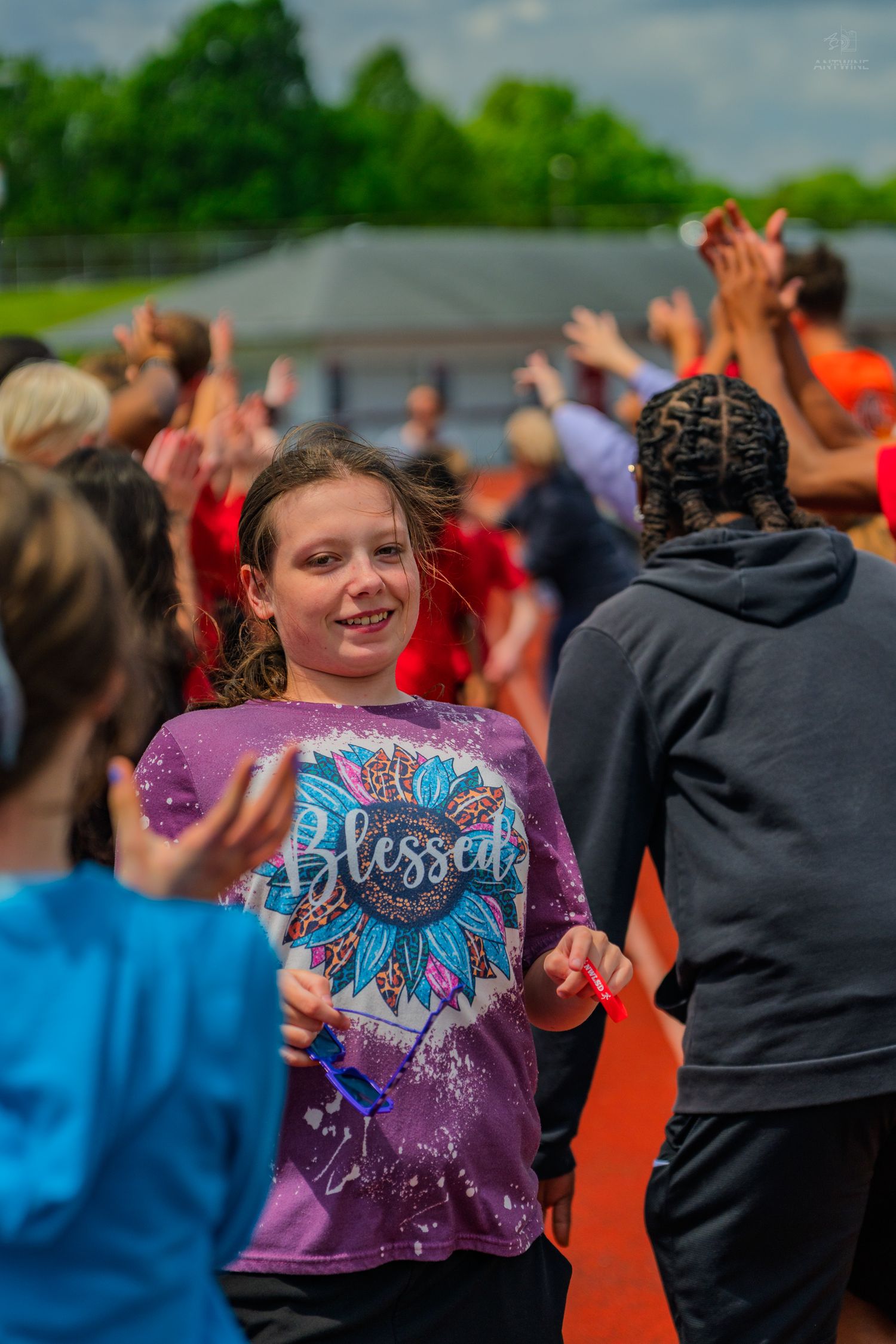 Smiling girl in a purple Blessed t-shirt walking through a high-five line at an outdoor school event.