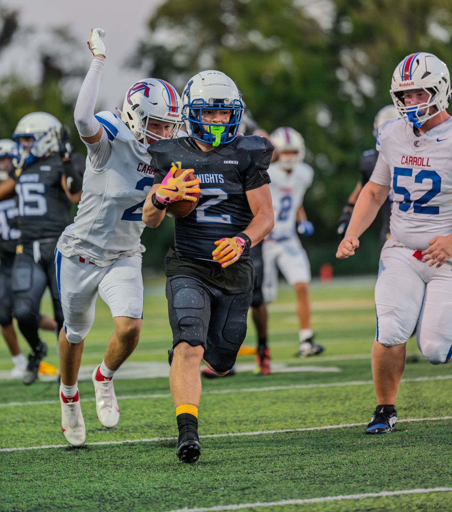 Knights football player number 2 in black uniform runs with the ball past Carroll defenders during a game.