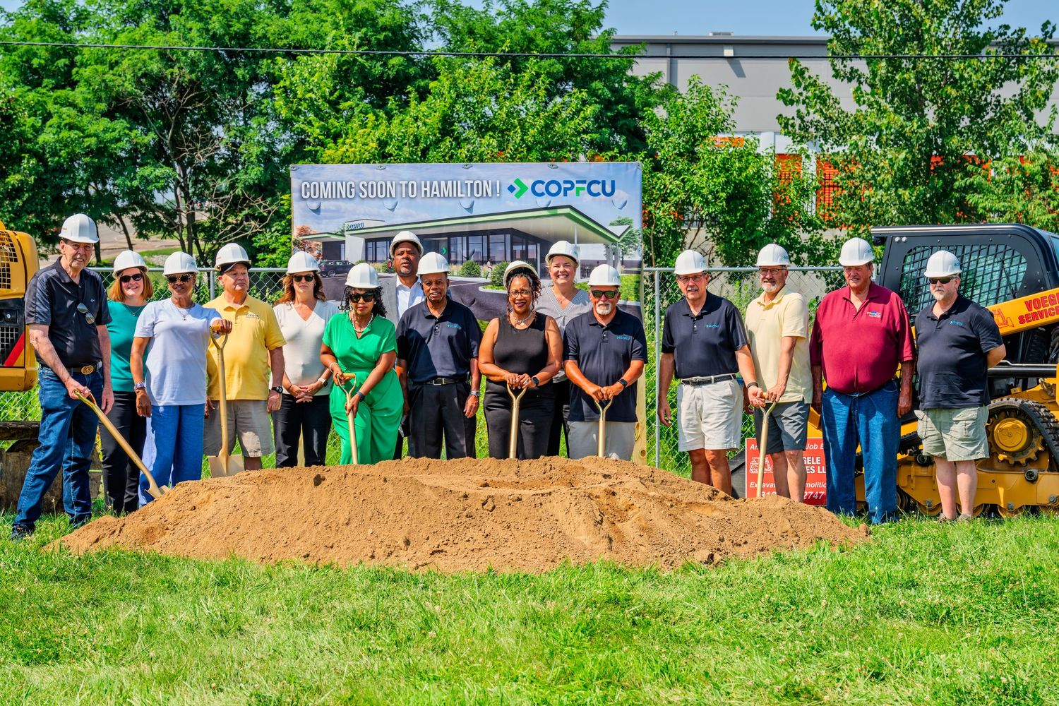 Group of people in white hard hats posing with golden shovels at COPCU Hamilton branch groundbreaking ceremony.