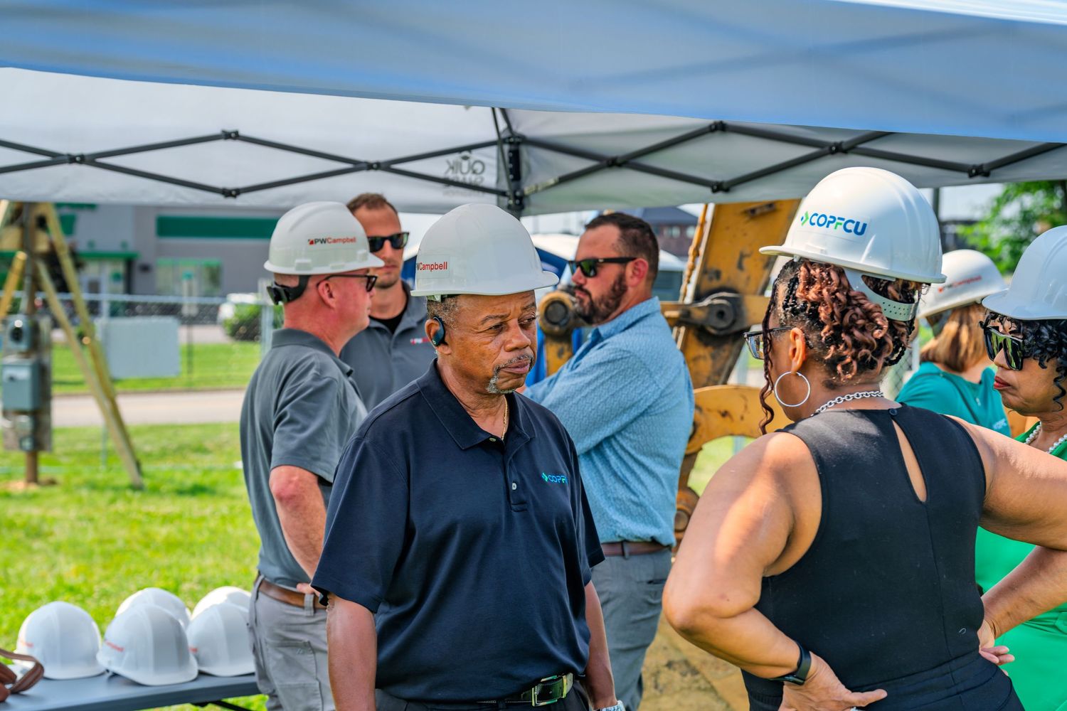 Group of people in hard hats having discussion under tent at COPCU credit union groundbreaking event.