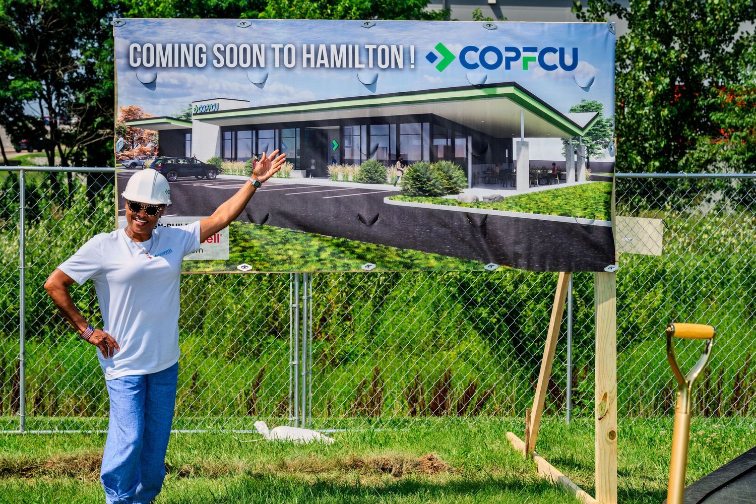 Person posing in front of COPFCU Coming Soon to Hamilton construction sign with golden shovel.