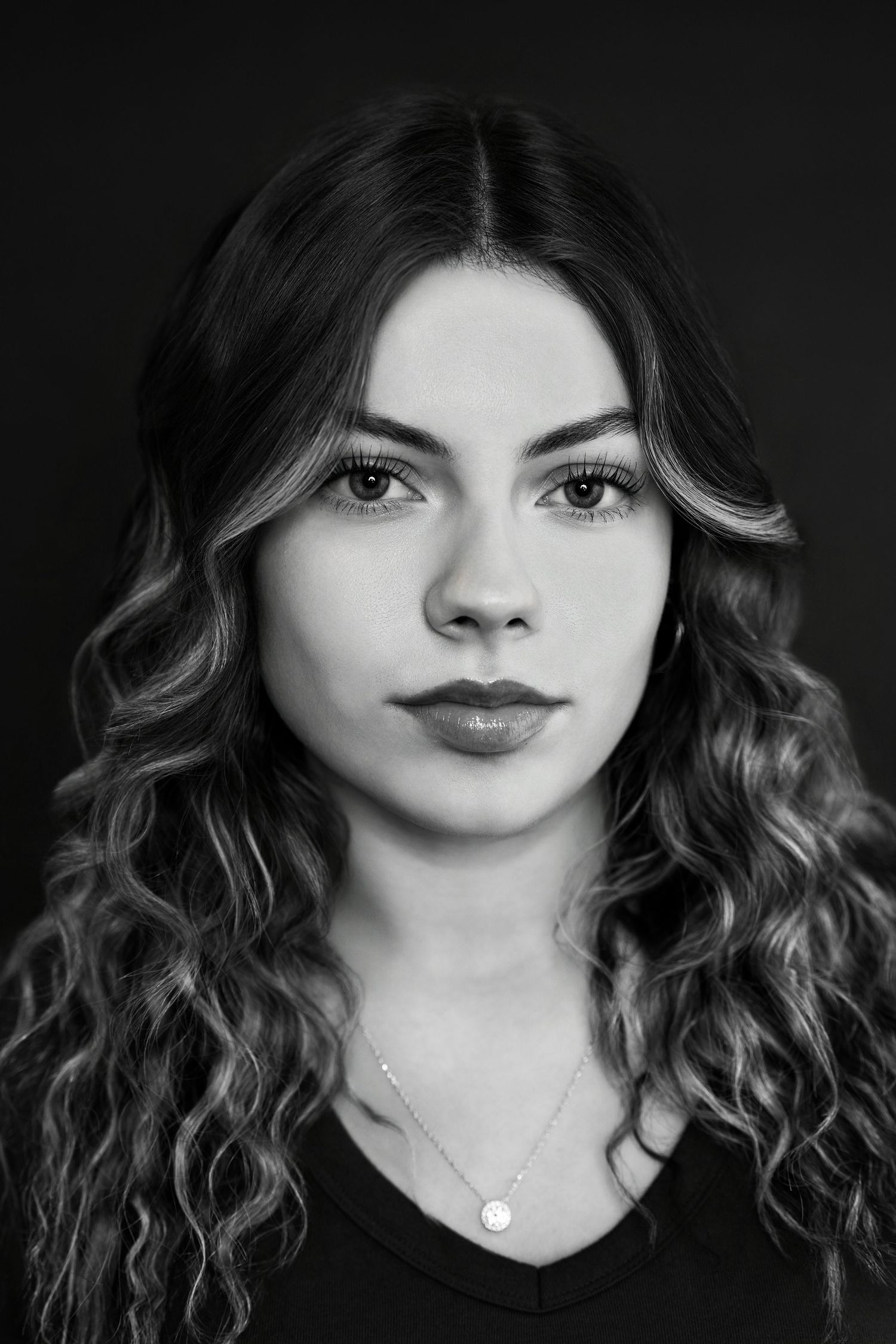 Striking black and white headshot of a young woman with long curly hair and a delicate necklace.