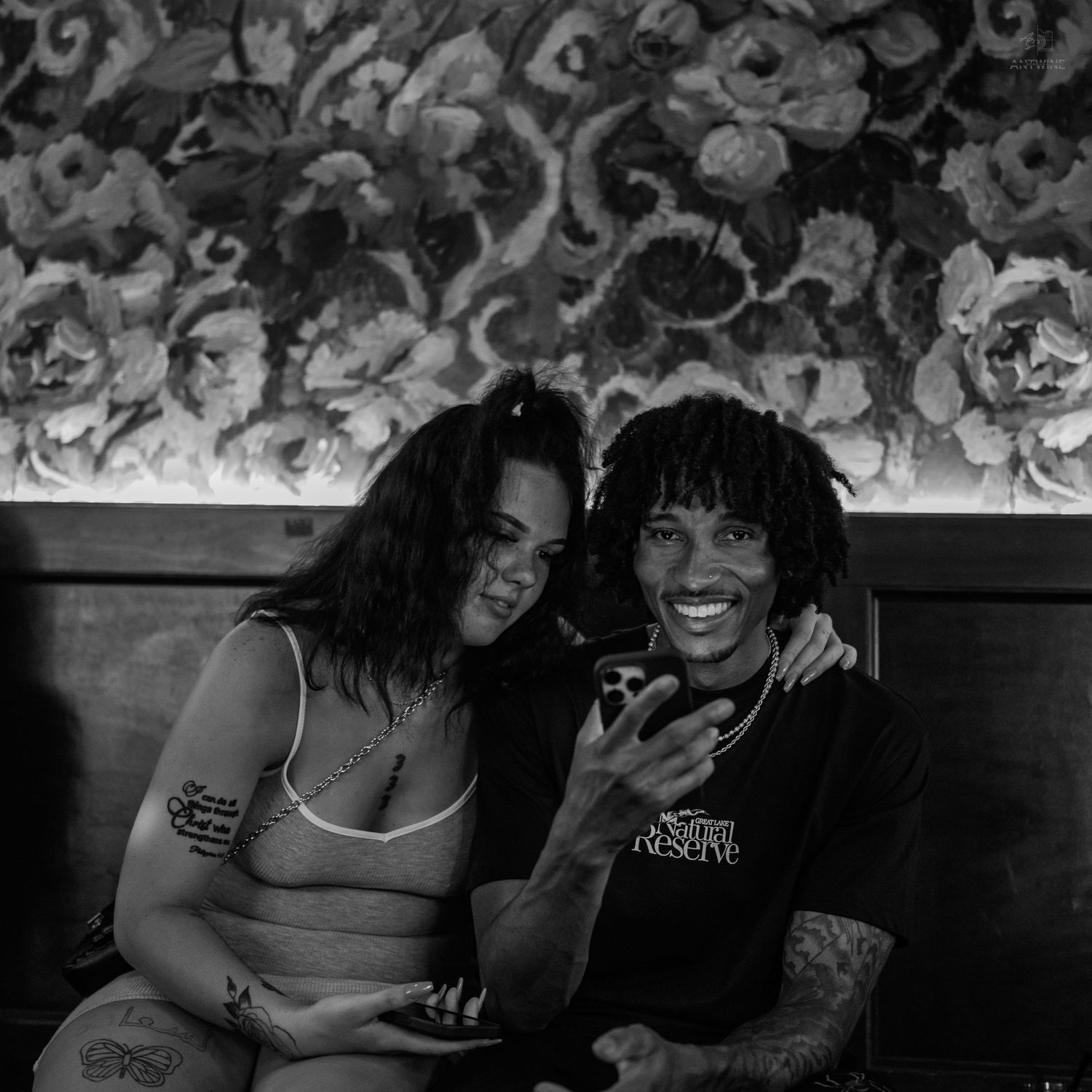 Black and white photo of two people sitting together on a couch in a dimly lit venue.