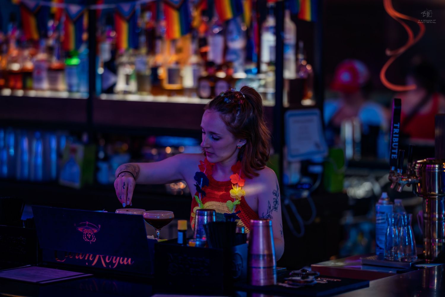 Female bartender working the register at a vibrant bar decorated with rainbow pride flags.