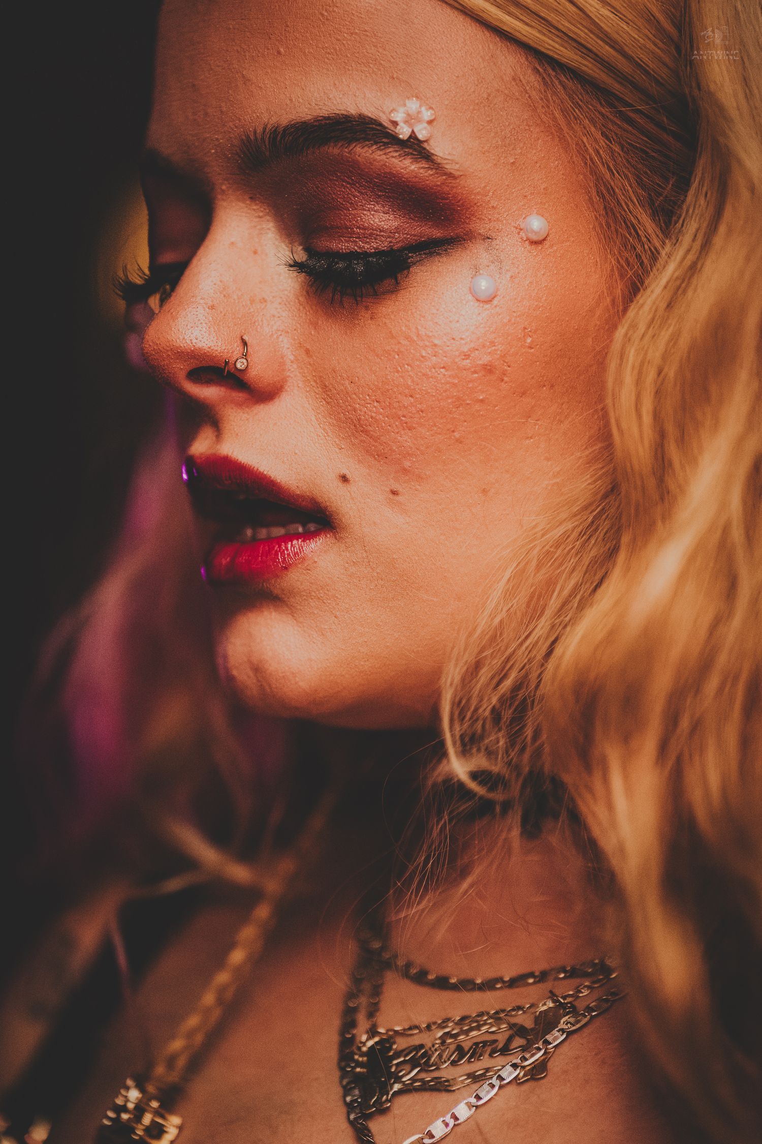 Close-up portrait of blonde woman with artistic festival makeup, floral gems, dramatic eye shadow, and red lips.